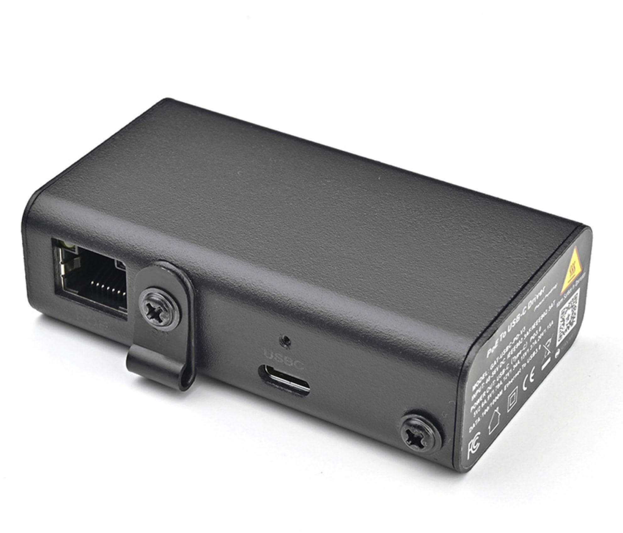 Ein schwarzes rechteckiges Gerät mit Ethernet-Anschluss, USB-C-Anschluss und Schrauben. Hat Etiketten und einen QR-Code.