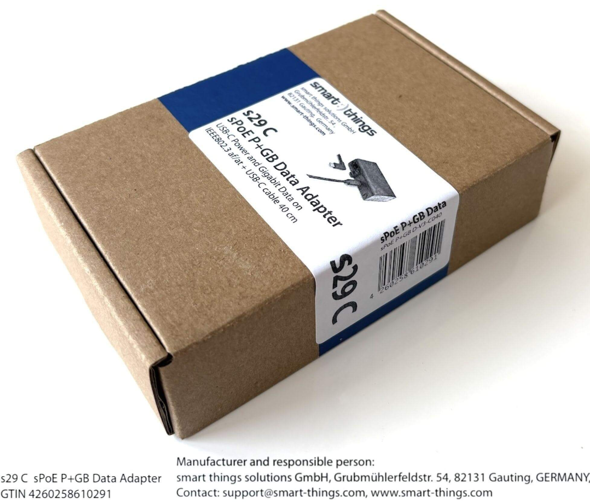 Brauner Karton mit weißen und blauen Etiketten. Text enthält Produktdetails und Firmeninformationen.