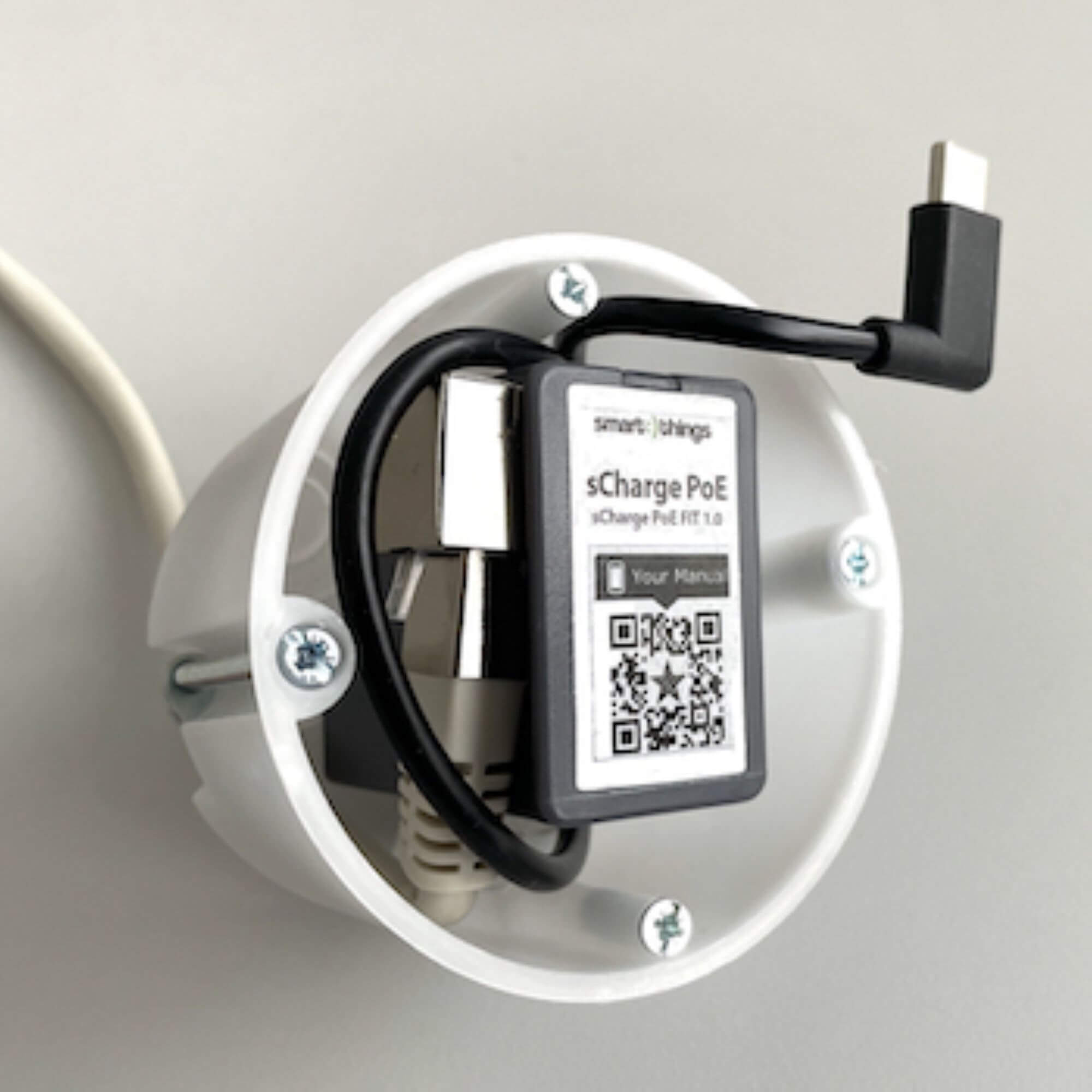 Weißes Wandgerät mit schwarzem Kabel und USB-C-Anschluss. In der Mitte befindet sich ein schwarzes und graues Gerät.