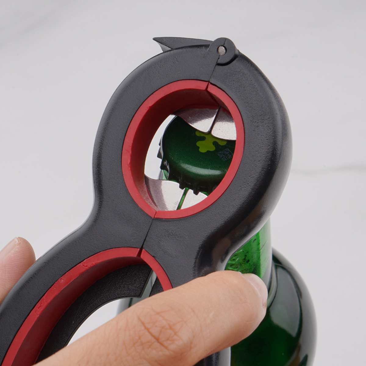 Eine Hand hält einen schwarz-roten Flaschenöffner und entfernt einen grünen Flaschenverschluss von einer grünen Flasche. Der Hintergrund ist unscharf.