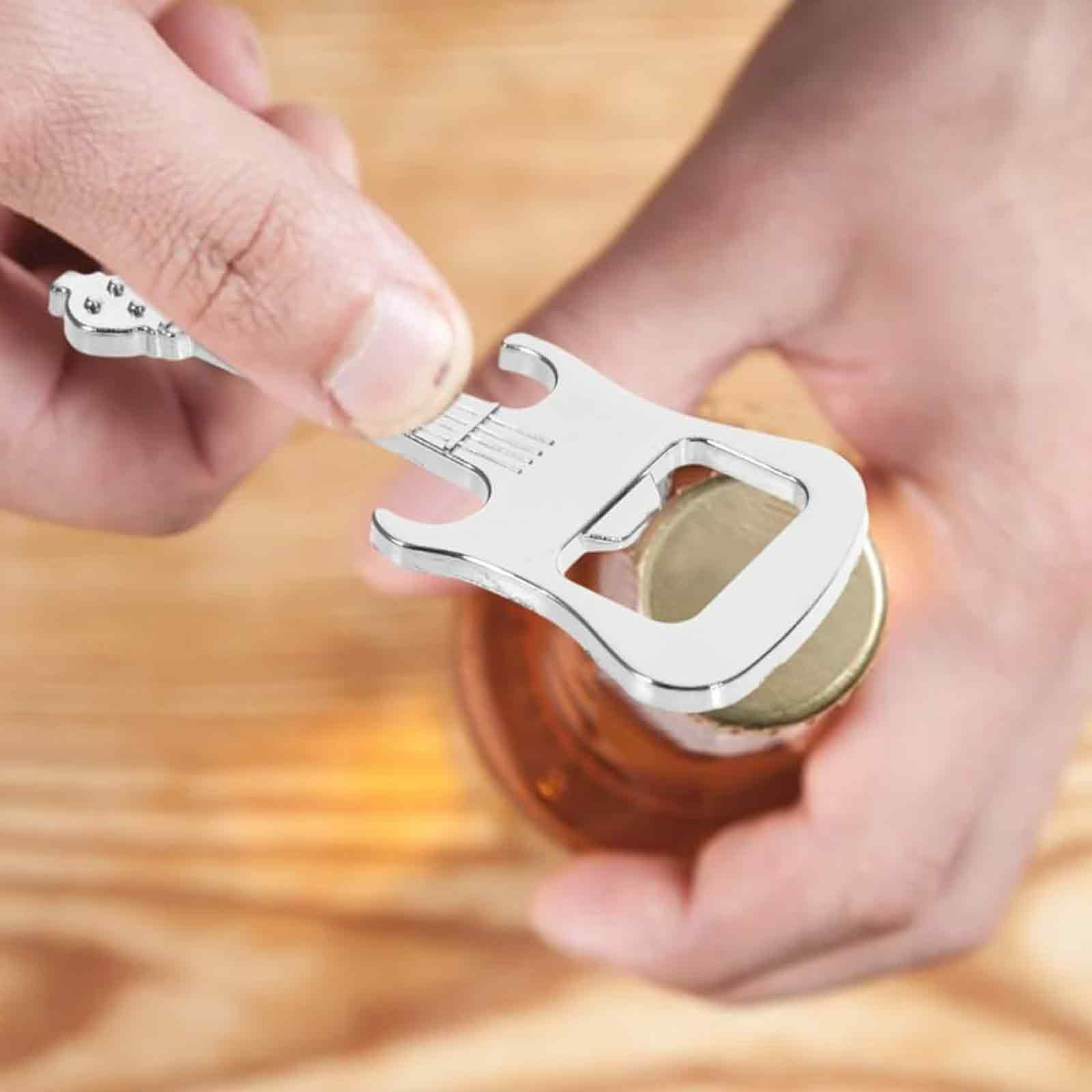 Eine Hand öffnet eine Flasche mit einem gitarrenförmigen Flaschenöffner. Der Öffner ist silber, die Flasche braun, die Oberfläche Holz.