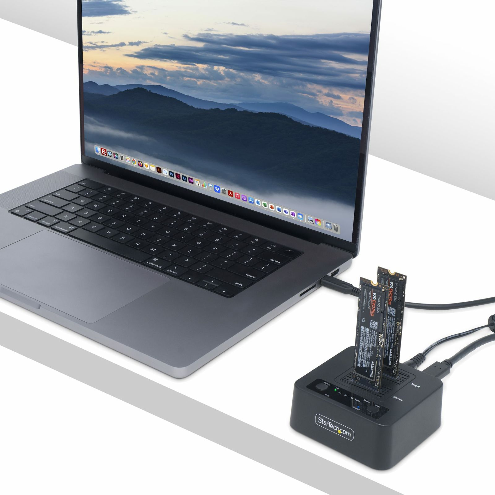 Ordenador portátil con lector SSD externo. La pantalla muestra un paisaje montañoso. Las SSD se insertan en el lector.