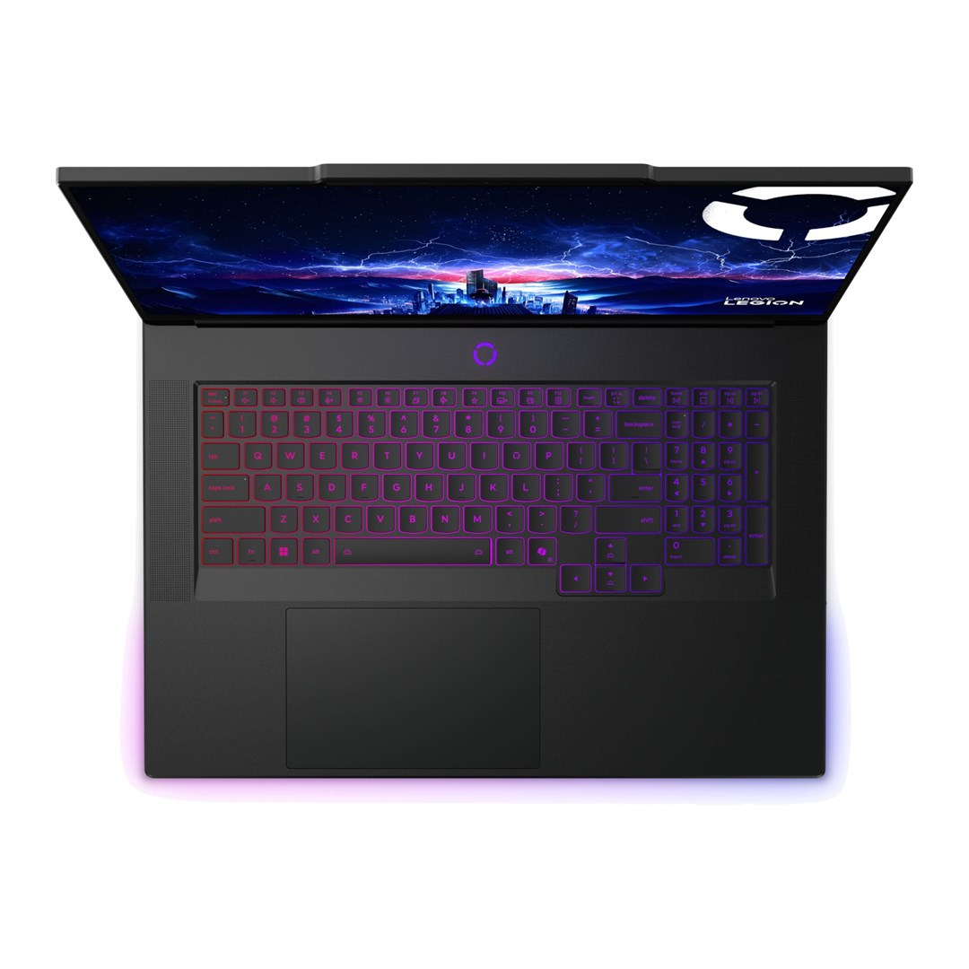 Czarny laptop z kolorową klawiaturą, otwarty na białej powierzchni, wyświetlający nocną scenerię. Widoczne słowo LEGION.