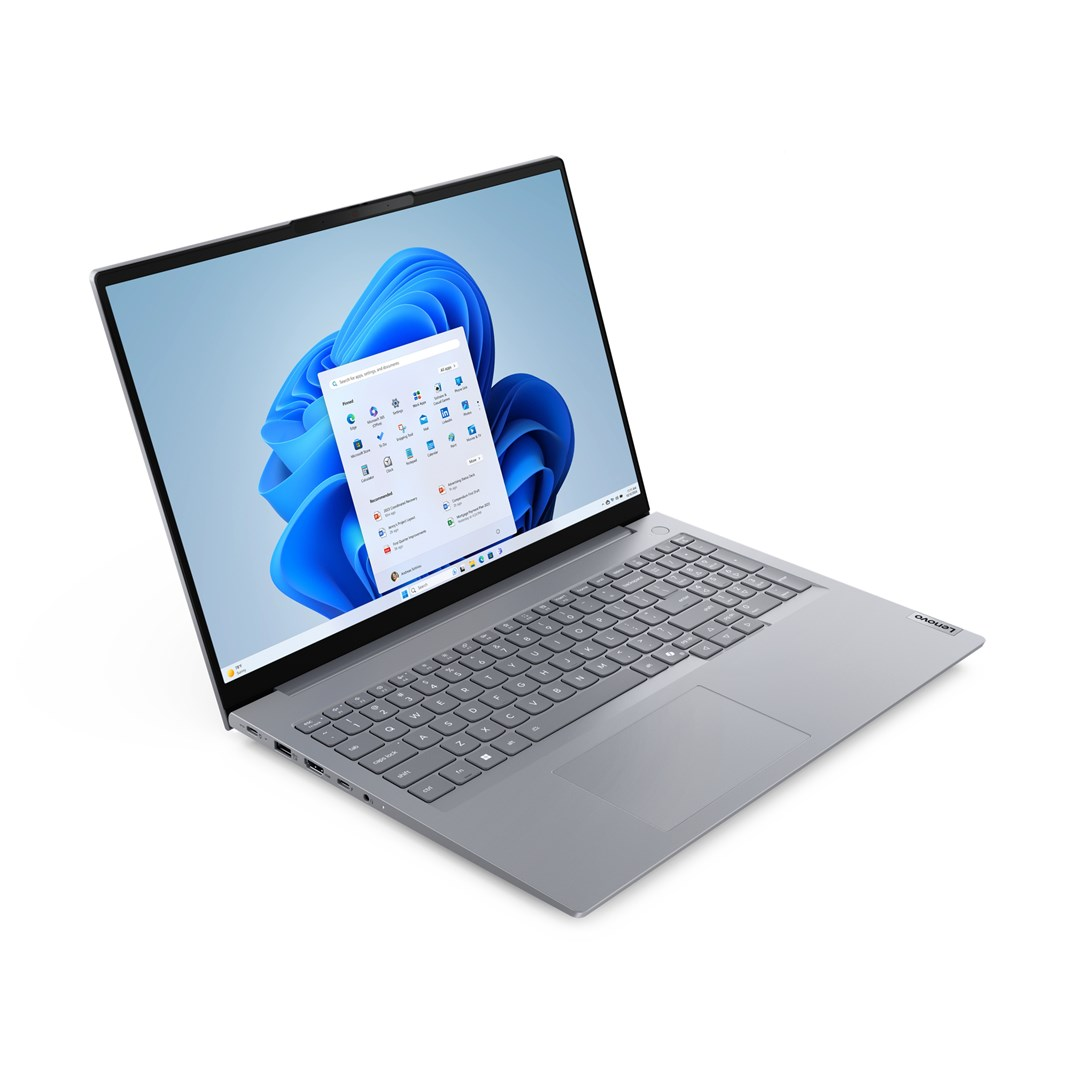 Szary laptop Lenovo jest otwarty, wyświetlając interfejs Windows 11. Ekran pokazuje menu start. Tło jest białe.