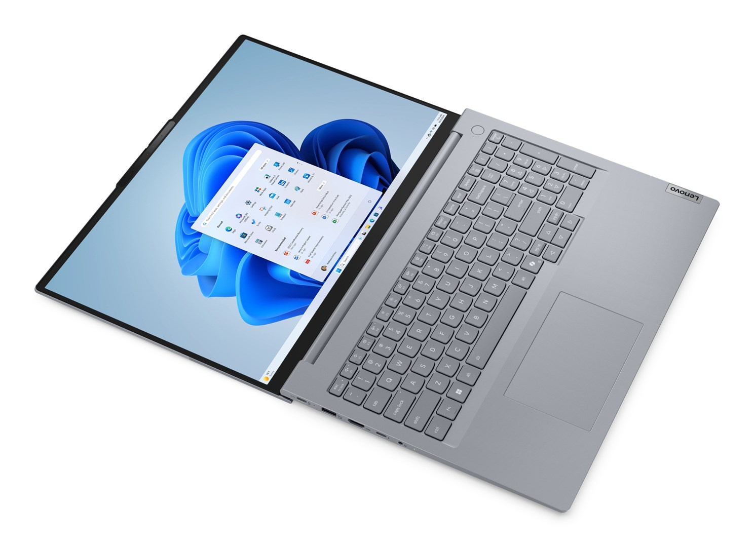 Laptop Lenovo jest otwarty. Ekran pokazuje interfejs Windows 11 na niebieskim tle. Klawiatura jest widoczna.