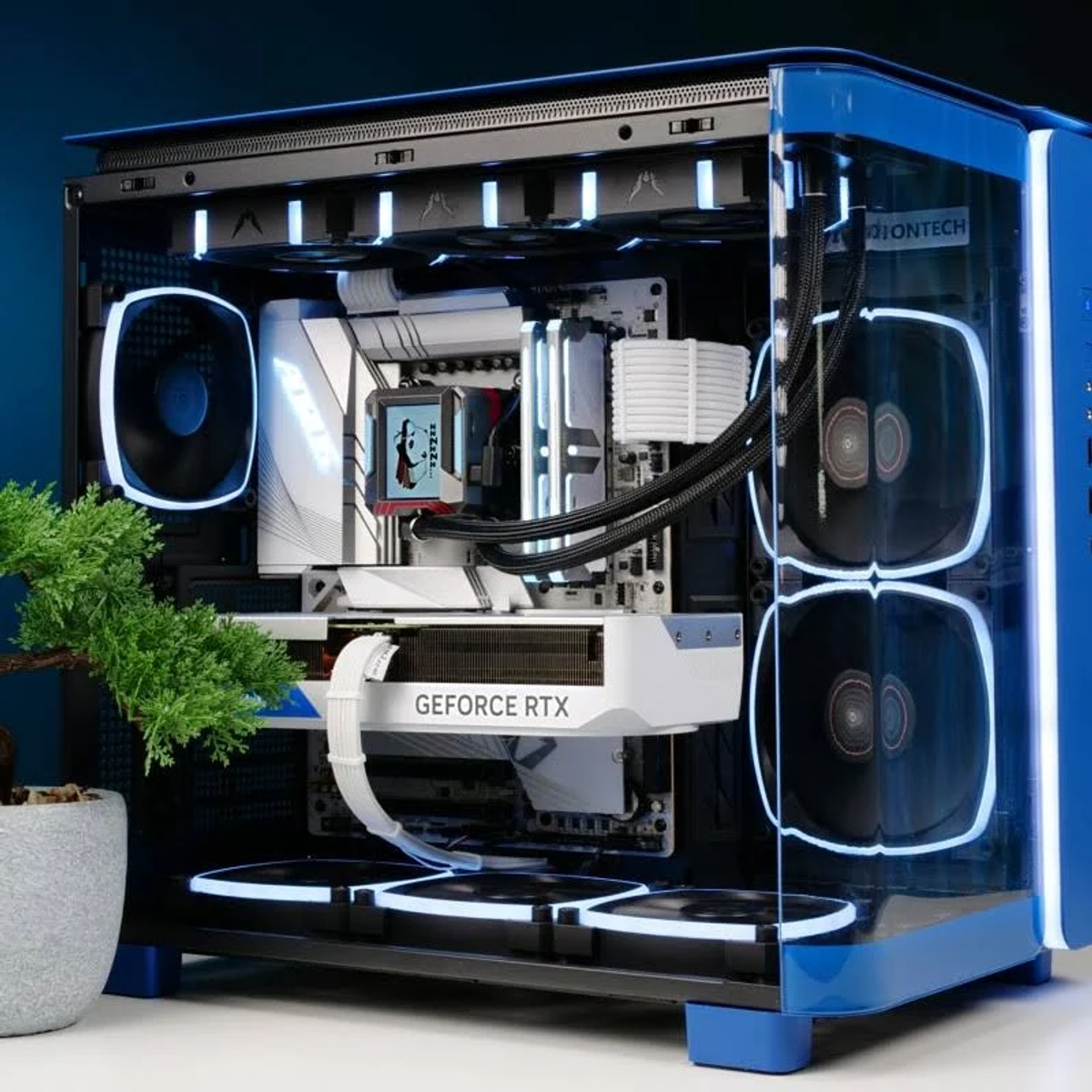 Un ordenador azul y blanco. Los componentes incluyen una tarjeta gráfica GeForce RTX y un pequeño bonsái.