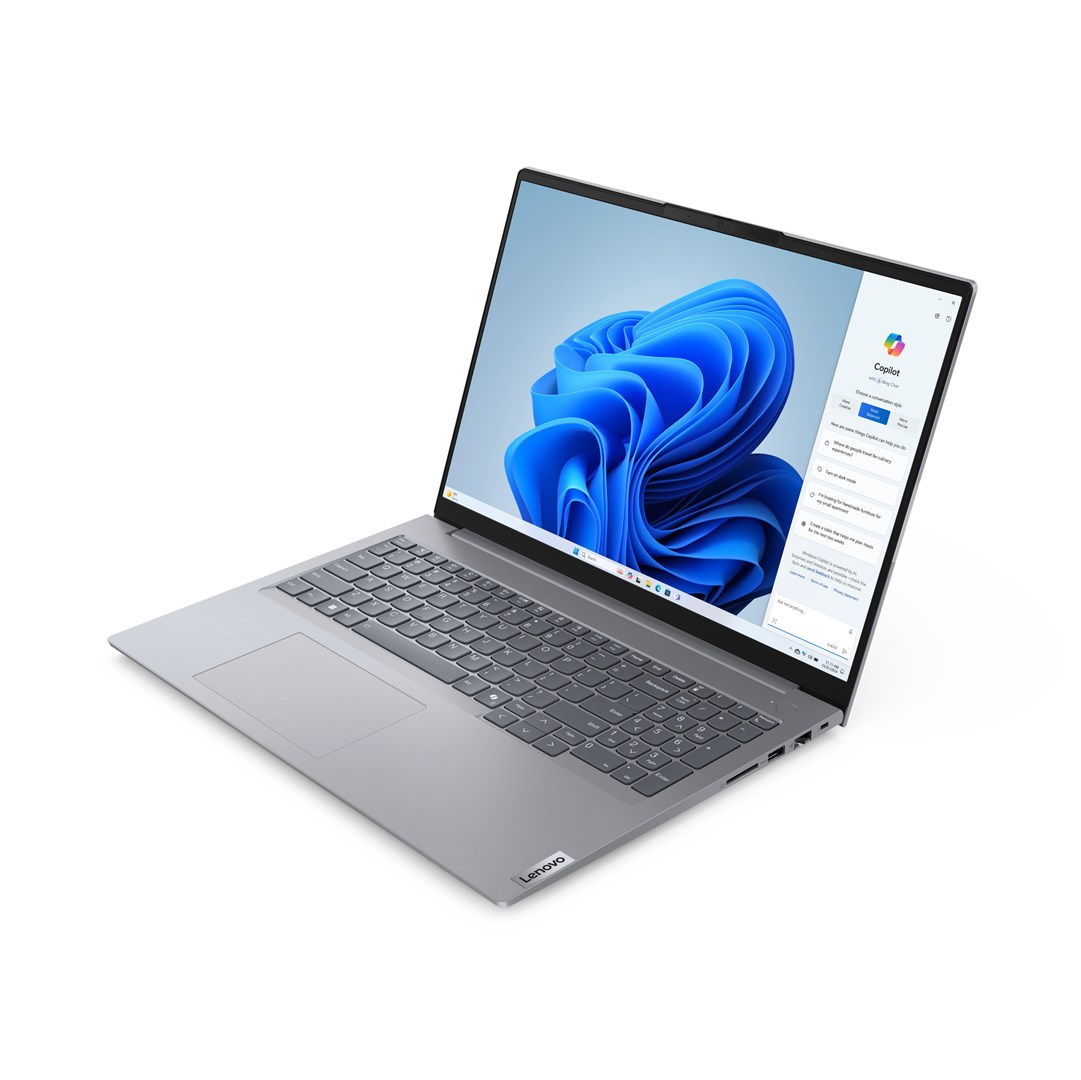 Laptop Lenovo jest otwarty, wyświetlając interfejs Windows 11. Ekran pokazuje niebieski abstrakcyjny wzór z otwartym panelem bocznym Copilot.
