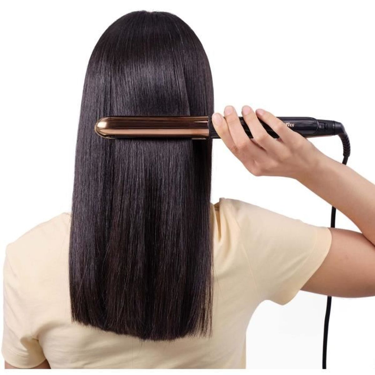 Una persona sta lisciando capelli lunghi e neri con una piastra. La persona indossa una maglietta gialla. Lo sfondo è bianco.
