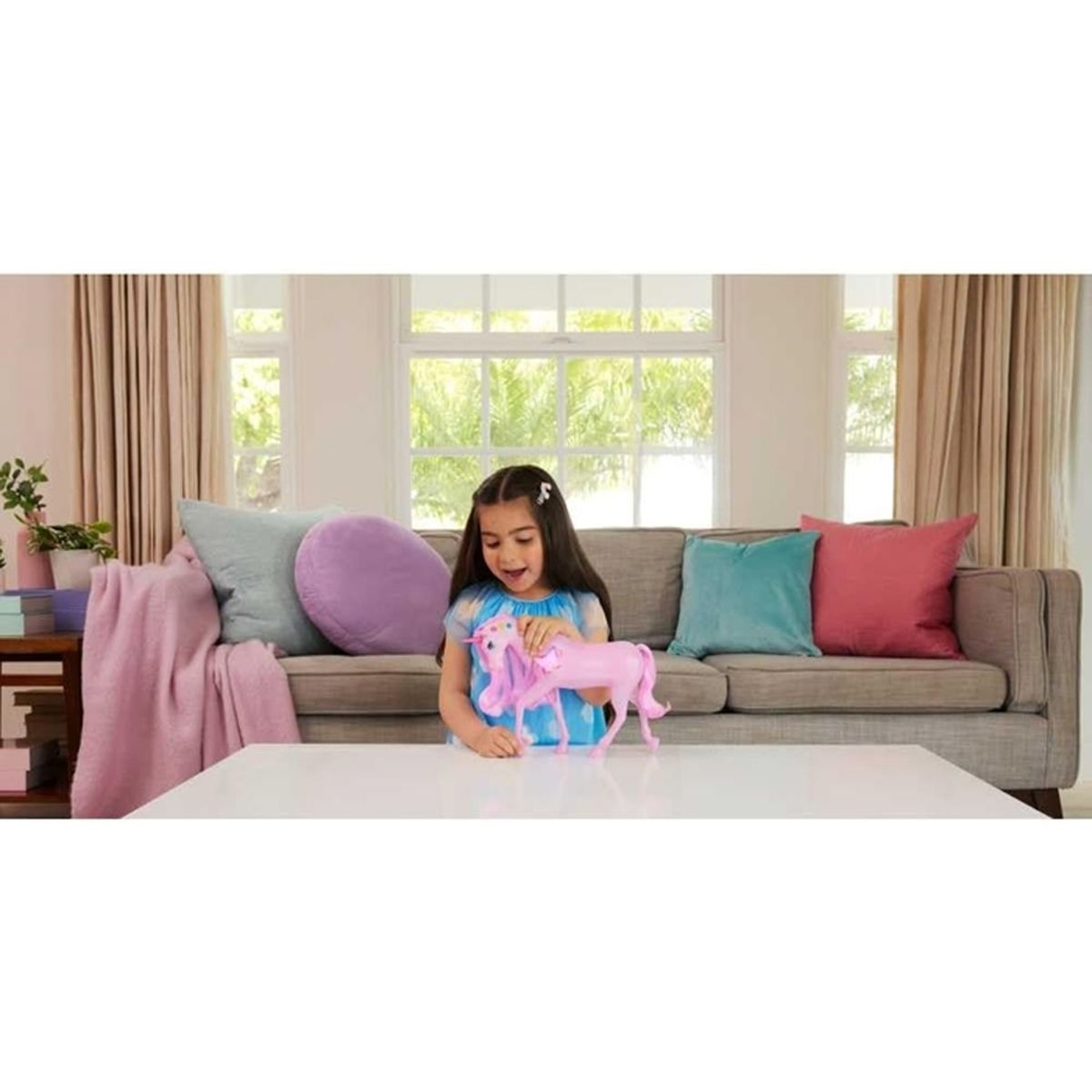 Ein Mädchen in einem blauen Kleid hält ein rosa Spielzeug-Einhorn. Im Hintergrund befindet sich eine Couch mit Kissen.