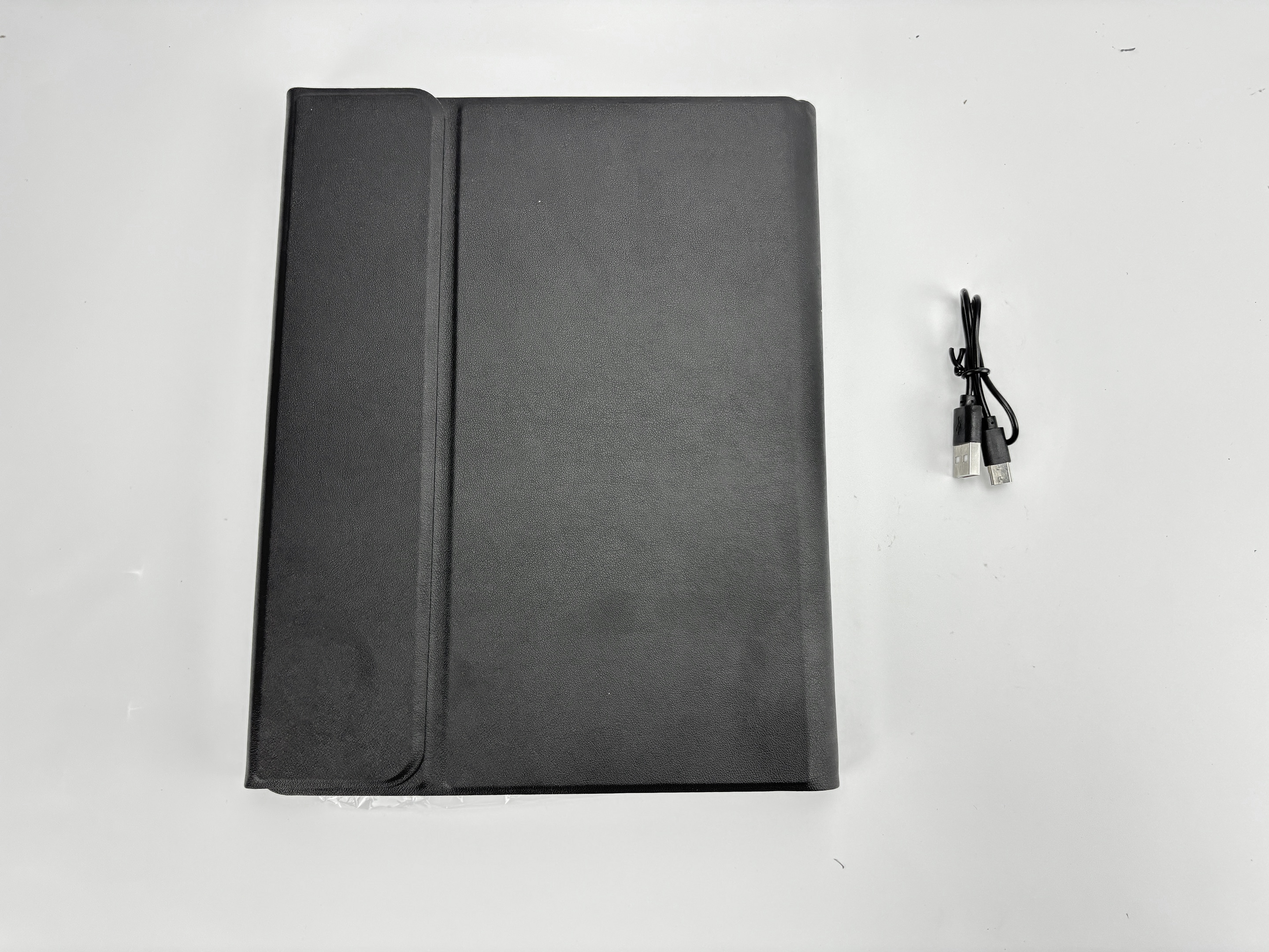 Auf einer weißen Oberfläche liegen eine schwarze Tablethülle und ein schwarzes Ladekabel.