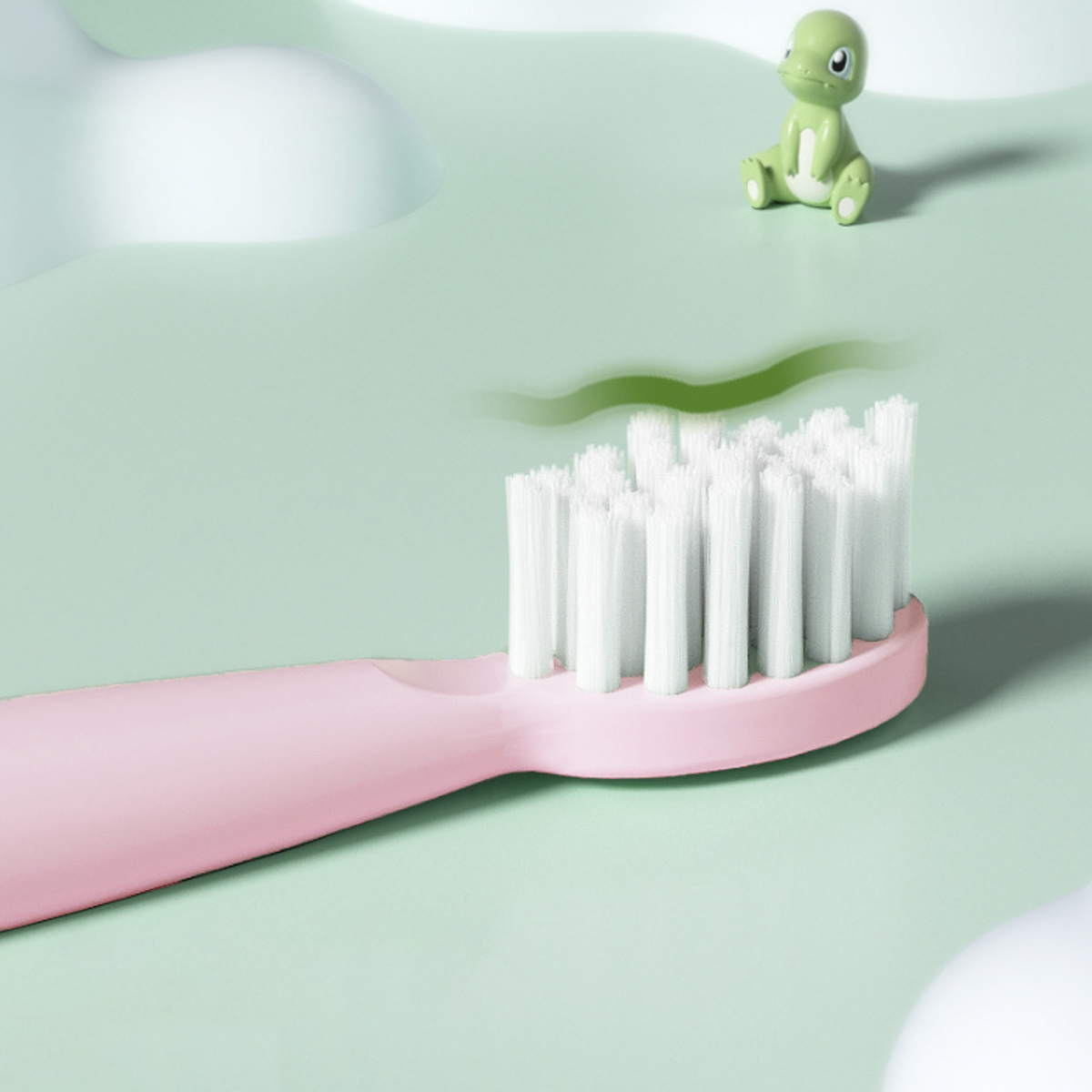 Eine rosa Zahnbürste mit weißen Borsten ist im Fokus. Ein grünes Dinosaurierspielzeug sitzt im Hintergrund. Der Hintergrund ist hellgrün.