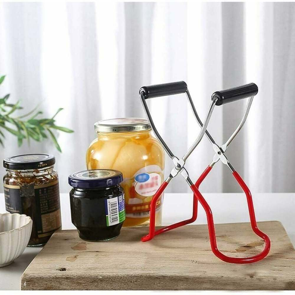 Ein Einmachgläserheber steht auf einem Holzbrett mit Gläsern. Gläser enthalten Marmelade und Obstkonserven. Weißer Vorhang im Hintergrund.