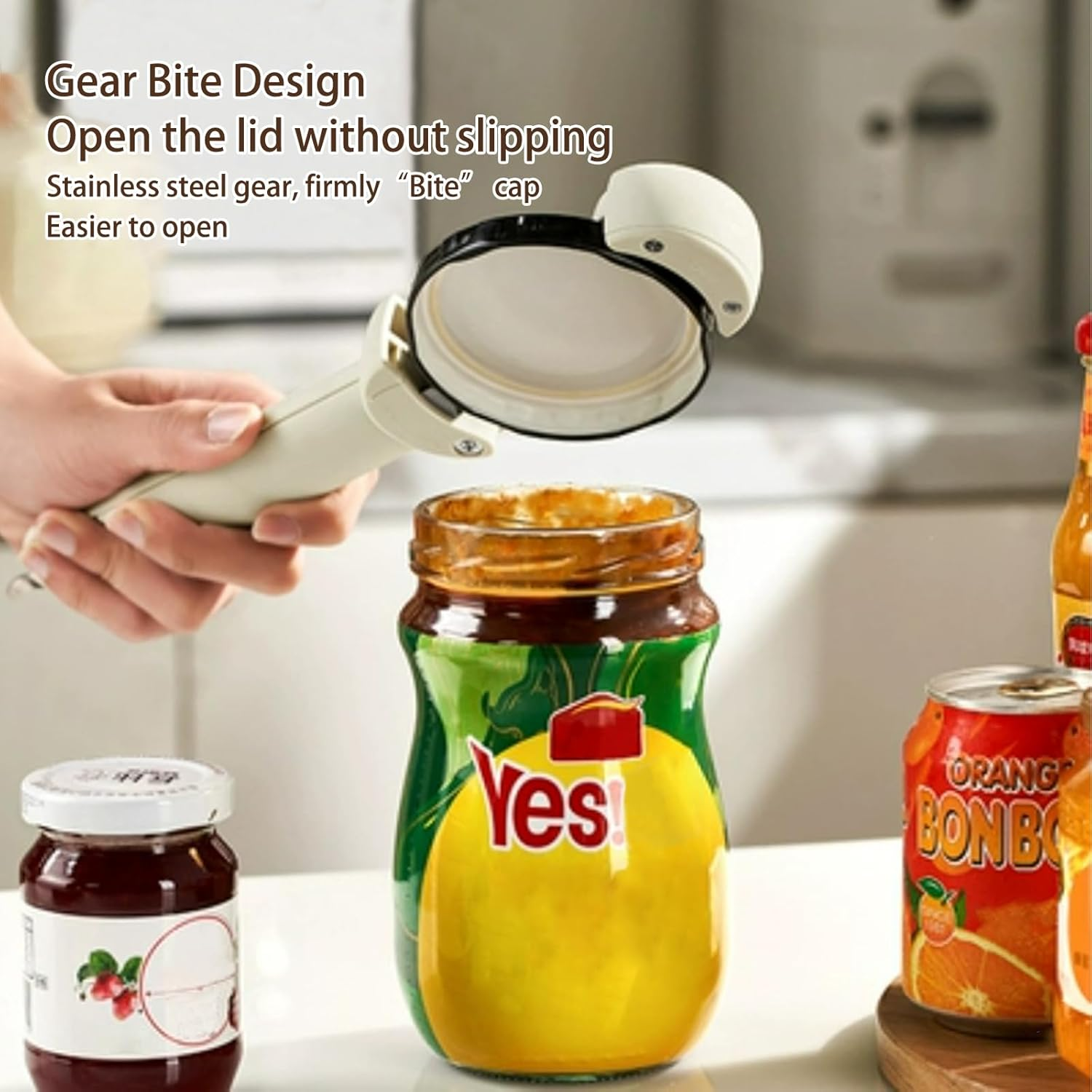 Eine Hand öffnet ein Glas mit einem Deckelöffner. Das Glas hat ein "Yes"-Etikett. Andere Gläser und eine Dose "Orange Bonbo" sind sichtbar.