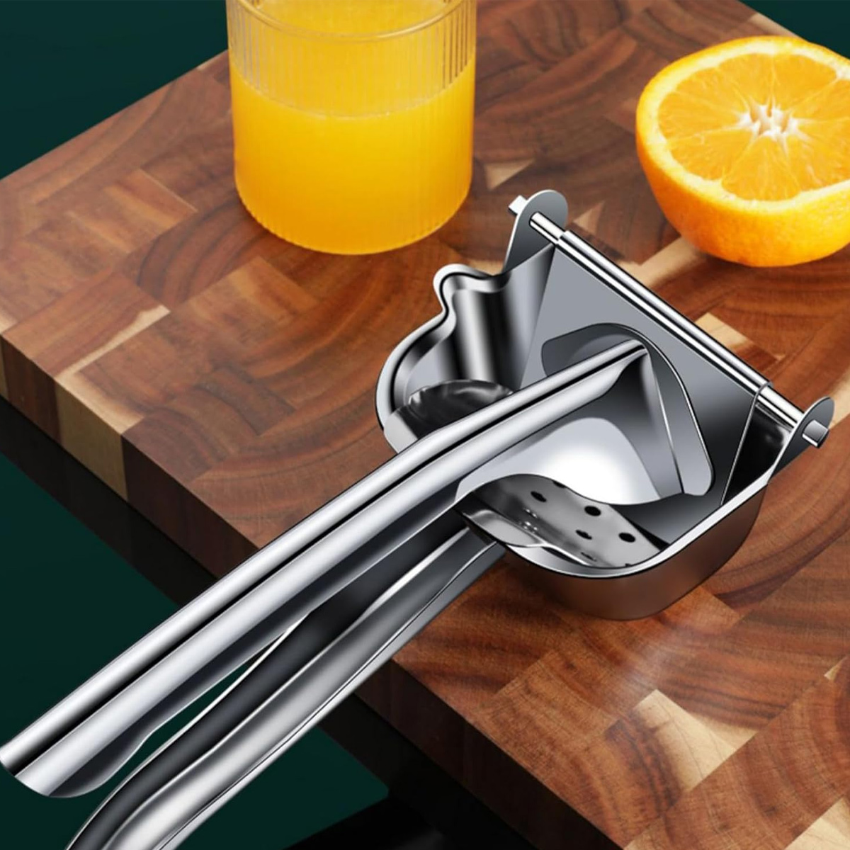 Ein Metall-Zitruspresser mit einer halbierten Orange und einem Glas Orangensaft auf einem Holzschneidebrett.