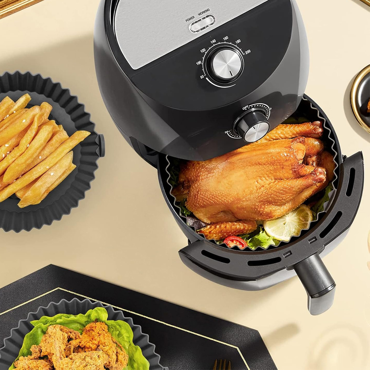 Ein Airfryer mit einem gebratenen Hähnchen, Pommes Frites und Hähnchen. Der Frittierer ist schwarz mit einem silbernen Deckel. Essen ist in schwarzen Schalen.