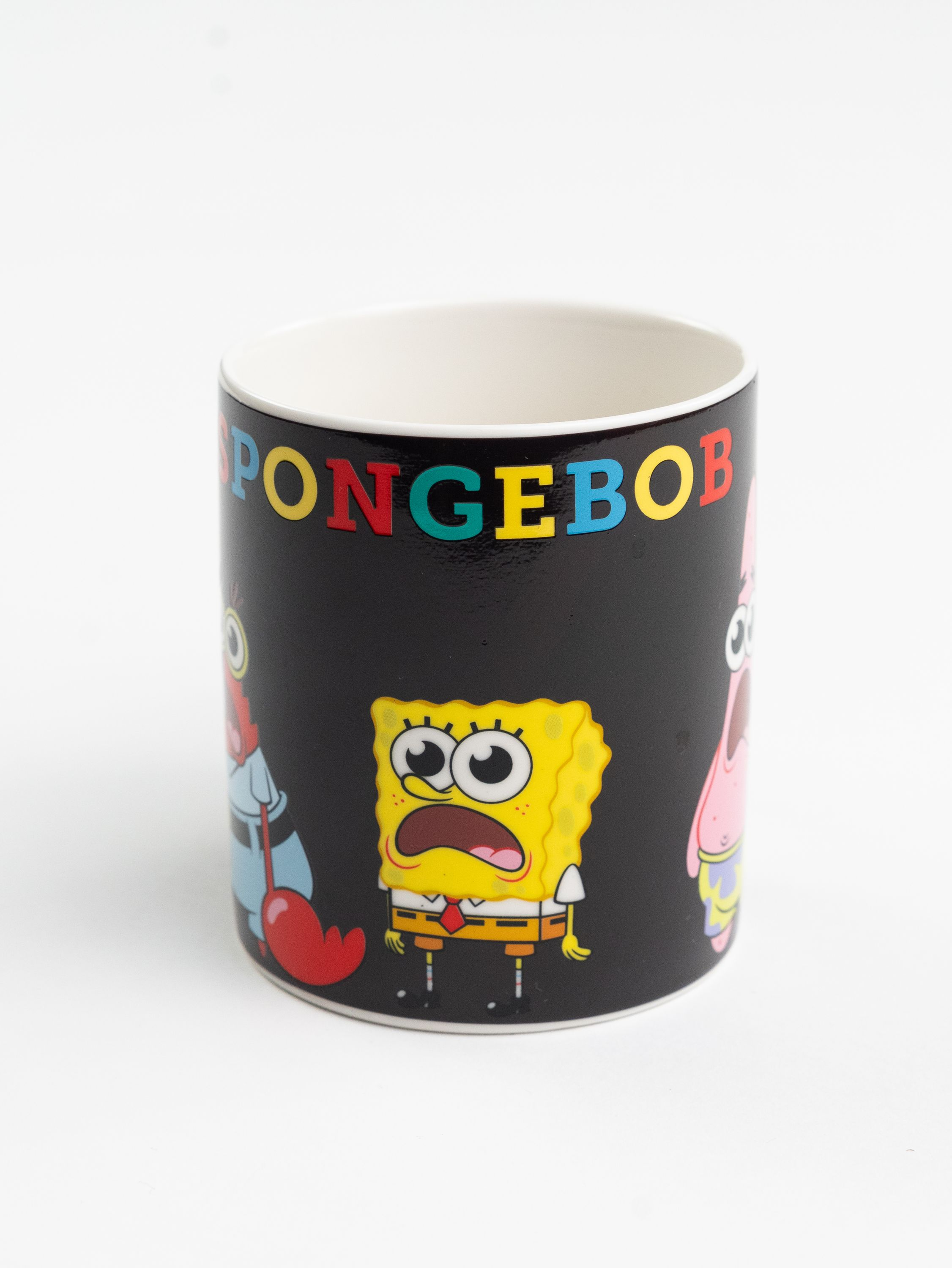 Eine Tasse mit SpongeBob-Figuren. Die Tasse ist schwarz mit bunten Buchstaben 'SPONGEBOB'.