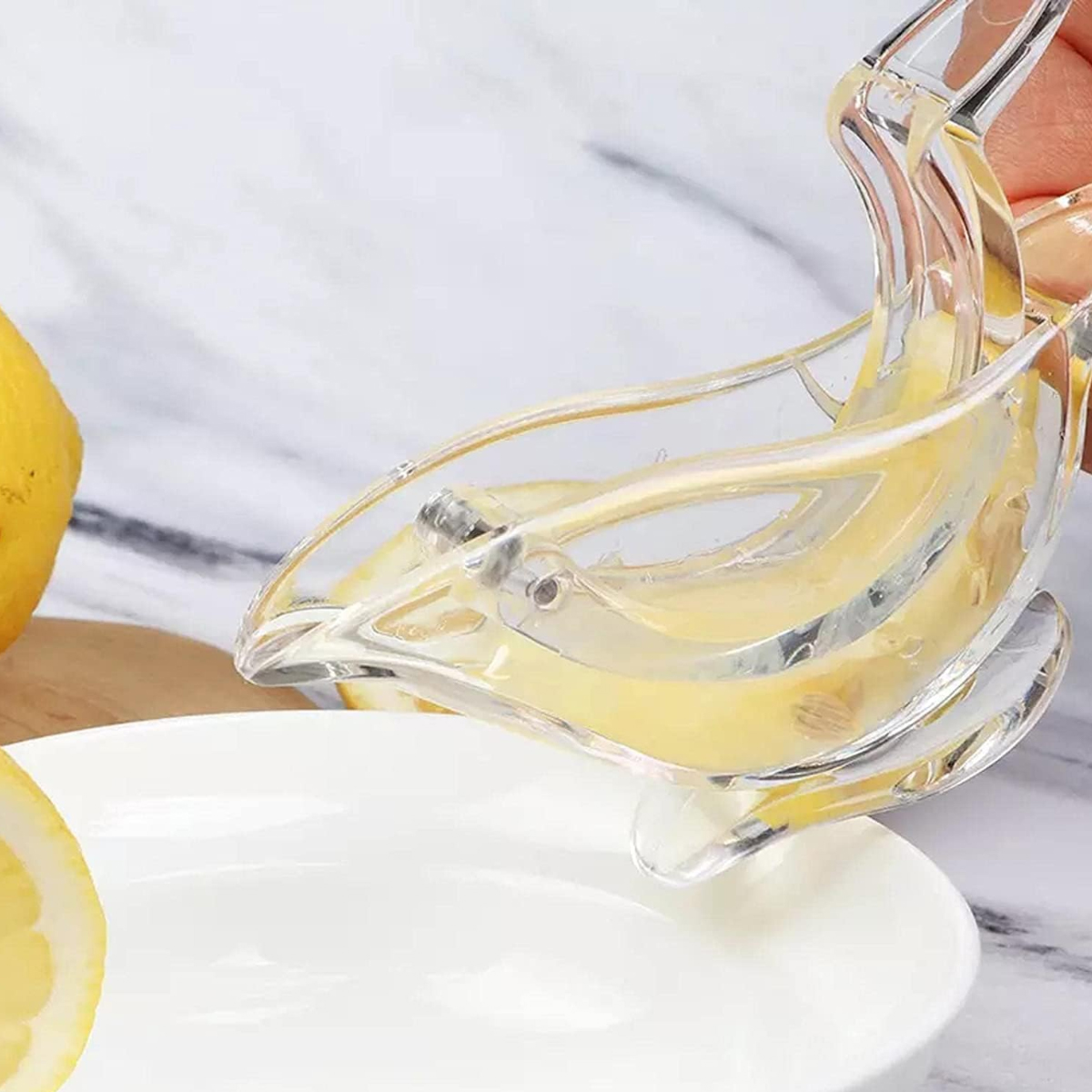 Ein klarer Zitronenentsafter mit Zitronenhälften. Saft fließt in einen weißen Teller. Eine ganze Zitrone ist im Hintergrund.