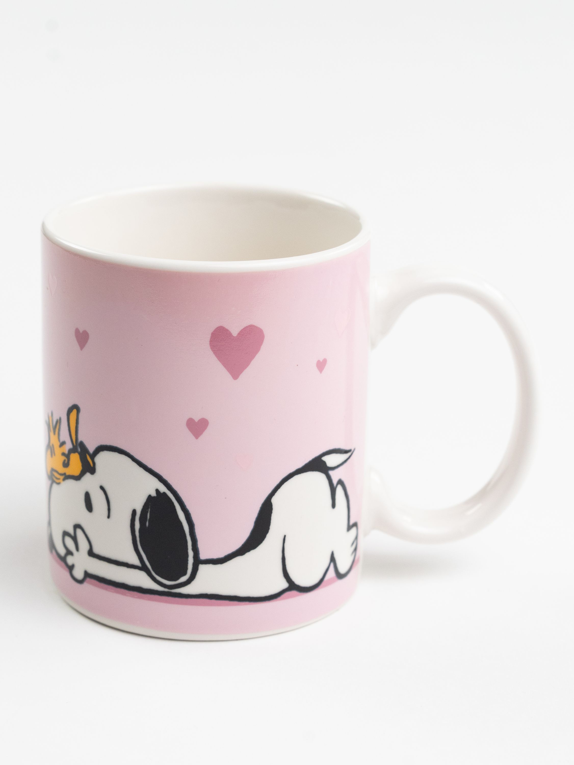 Rosa Tasse mit Snoopy-Illustration und Herzen. Weißer Henkel und Innenraum. Weißer Hintergrund.