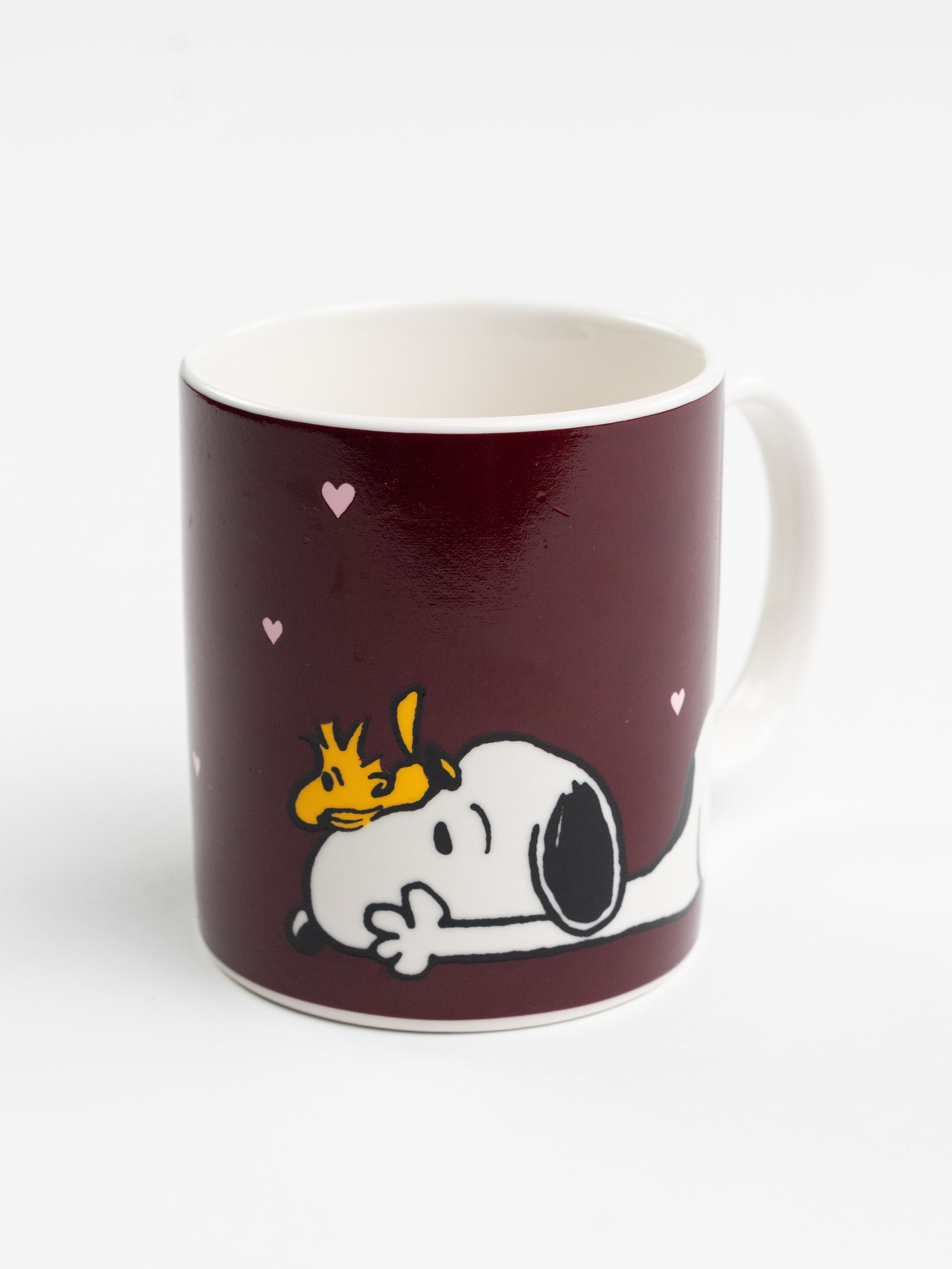 Eine Tasse mit Snoopy und Woodstock. Die Tasse ist weinrot mit rosa Herzen. Weißes Innere und Griff.