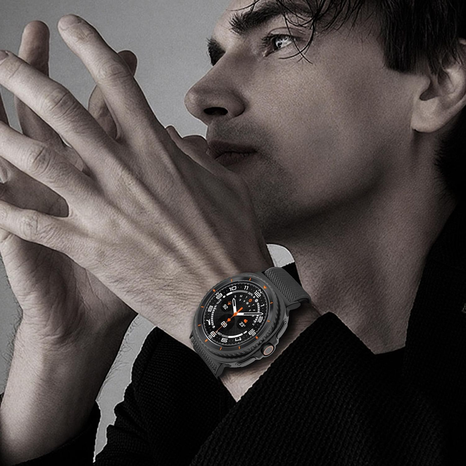 Un uomo indossa uno smartwatch nero. L'orologio ha un cinturino nero e un quadrante nero con dettagli arancioni. L'uomo guarda altrove.