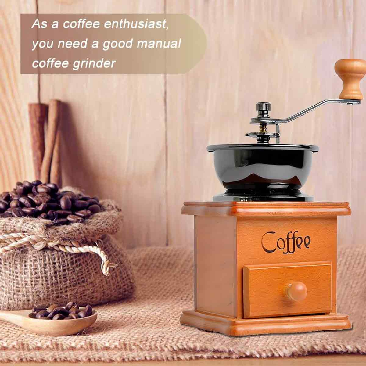 Eine manuelle Kaffeemühle steht auf einem Holzsockel. Ein Sack Kaffeebohnen und ein Holzlöffel sind im Vordergrund.