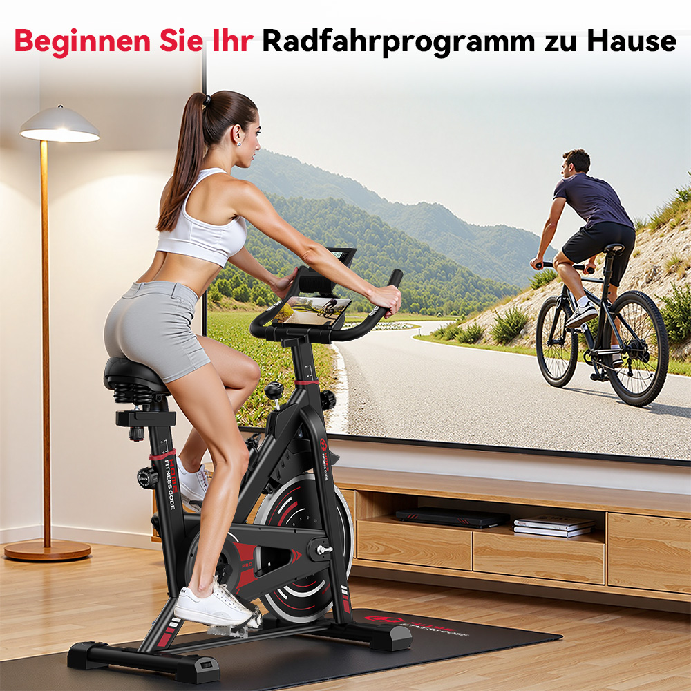 Kobieta na rowerze stacjonarnym, telewizor pokazuje mężczyznę jeżdżącego na rowerze na zewnątrz. Pokój ma drewnianą podłogę i lampę. Rower jest czarny i czerwony.