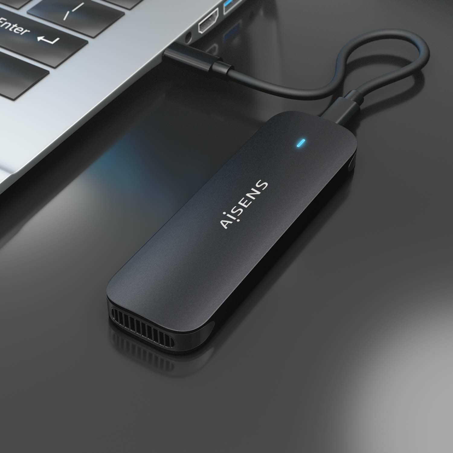 Un disco duro externo Aisens negro está conectado a una computadora portátil. La unidad tiene una luz azul y un cable se conecta a la computadora portátil.