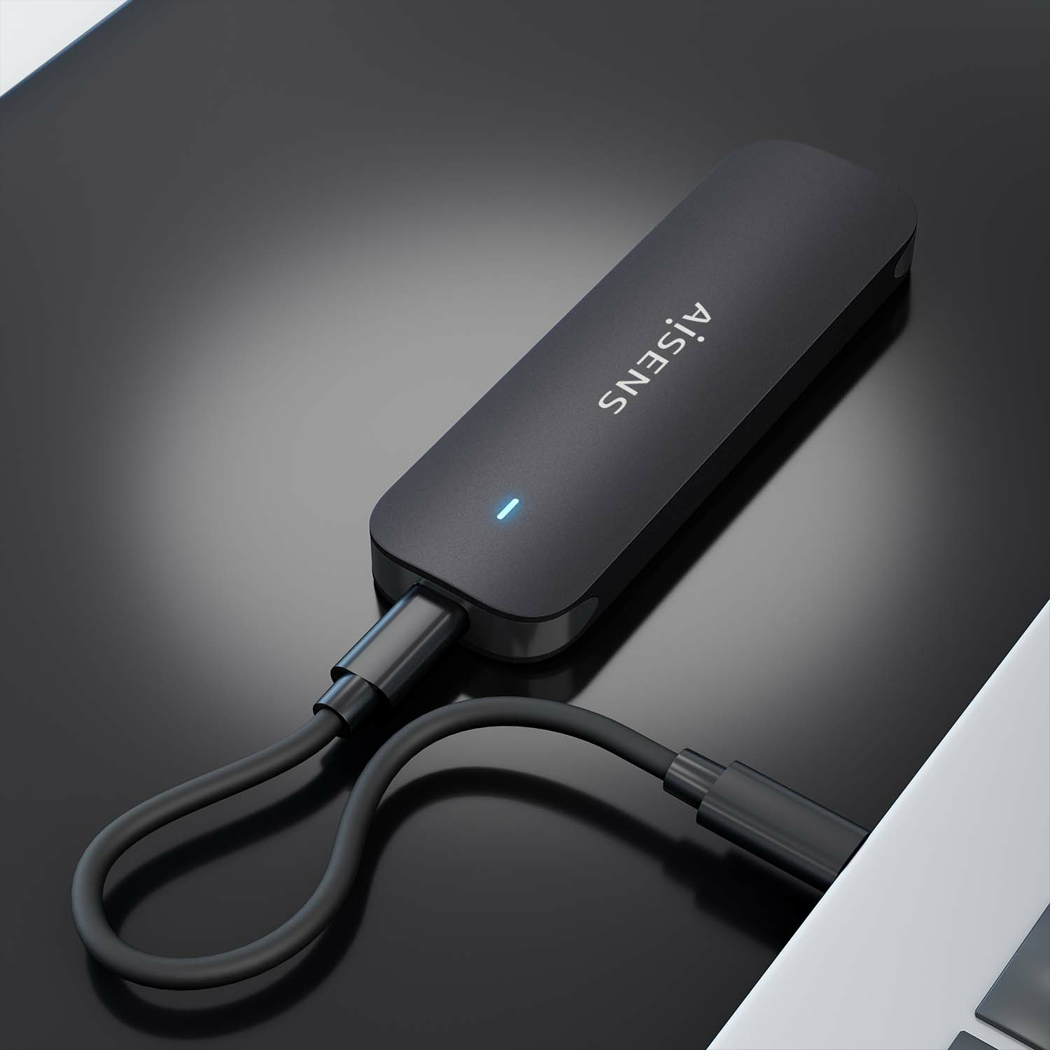 Un dispositivo AISENS negro con un cable conectado a una computadora portátil. El dispositivo está sobre una superficie negra reflectante.