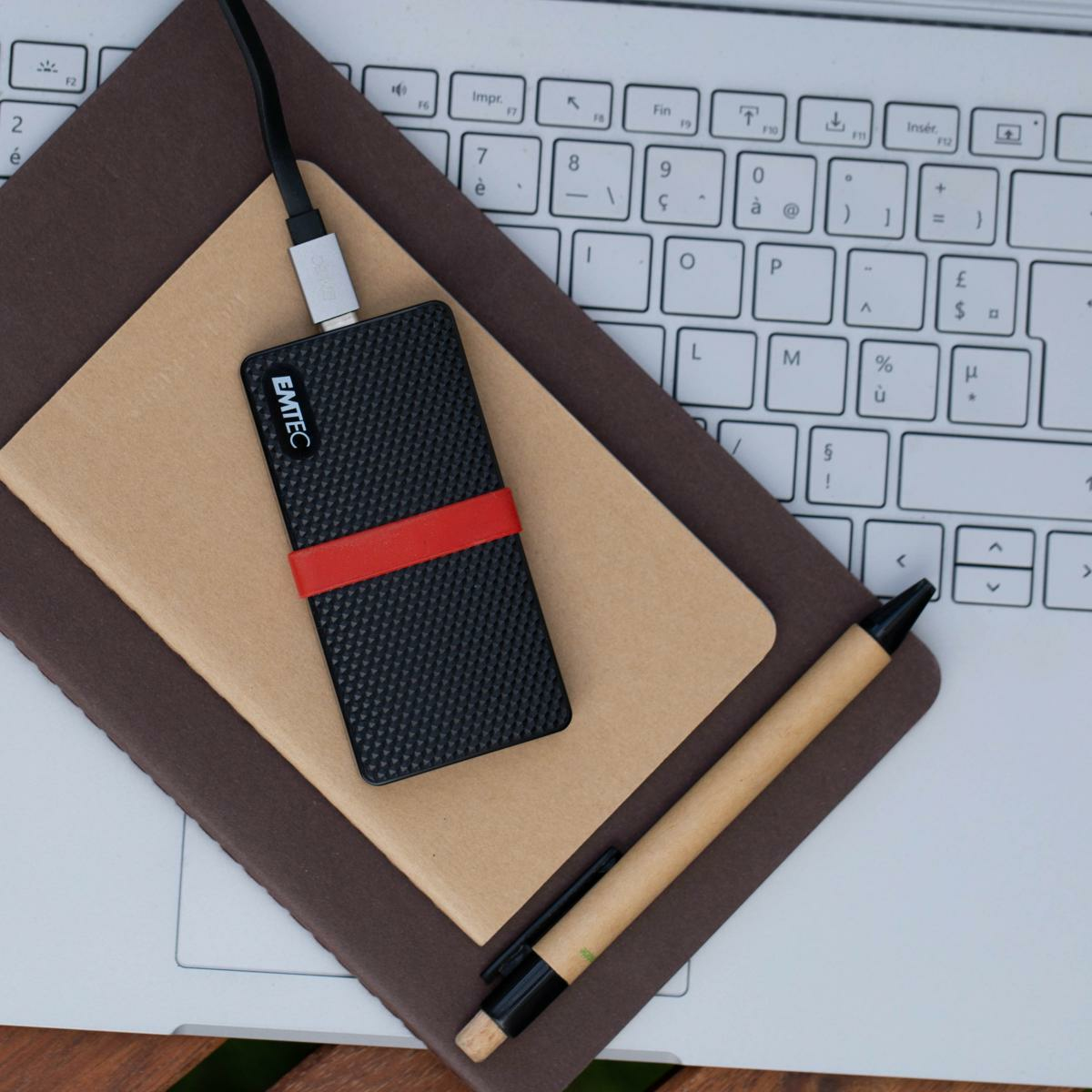 Czarny dysk twardy z czerwonym paskiem na notatnikach i długopis, na klawiaturze laptopa.