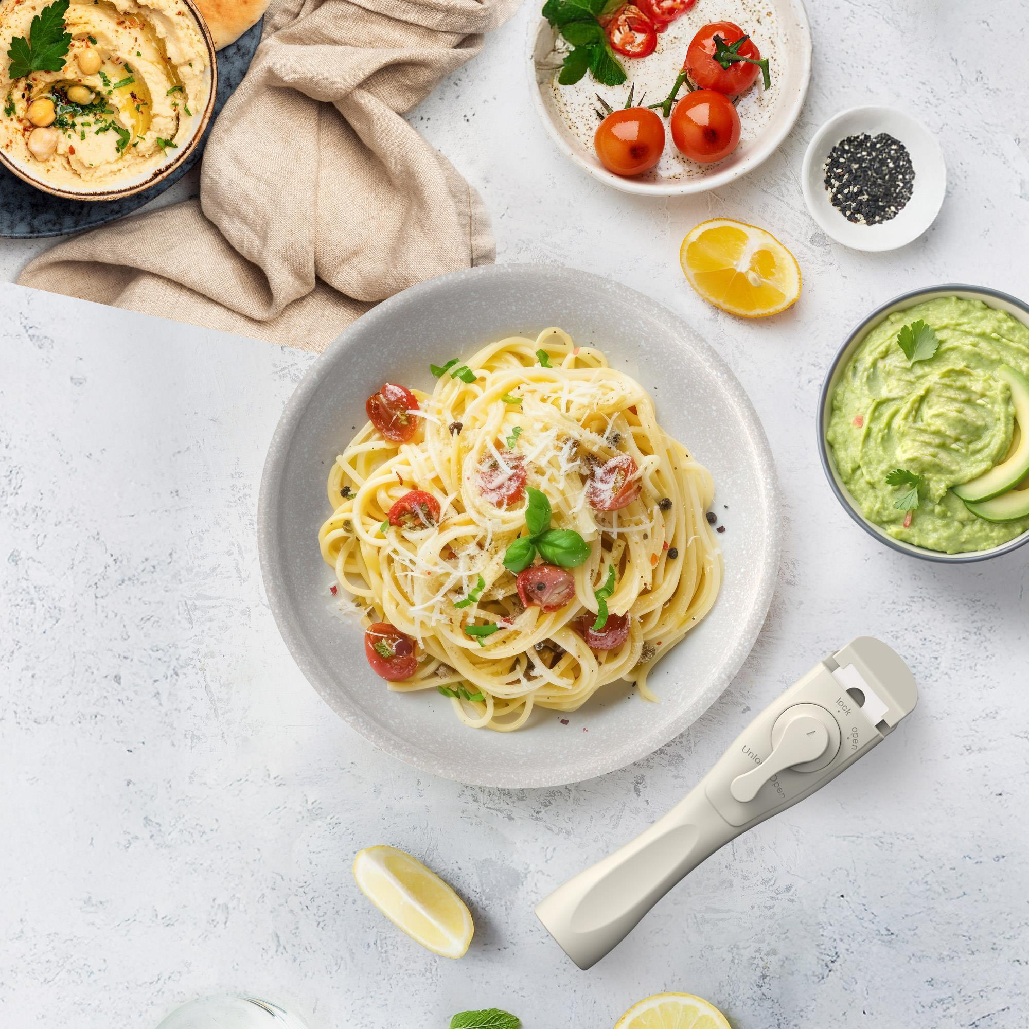 Vista aérea de una comida con pasta, hummus, tomates, aguacate y limones.