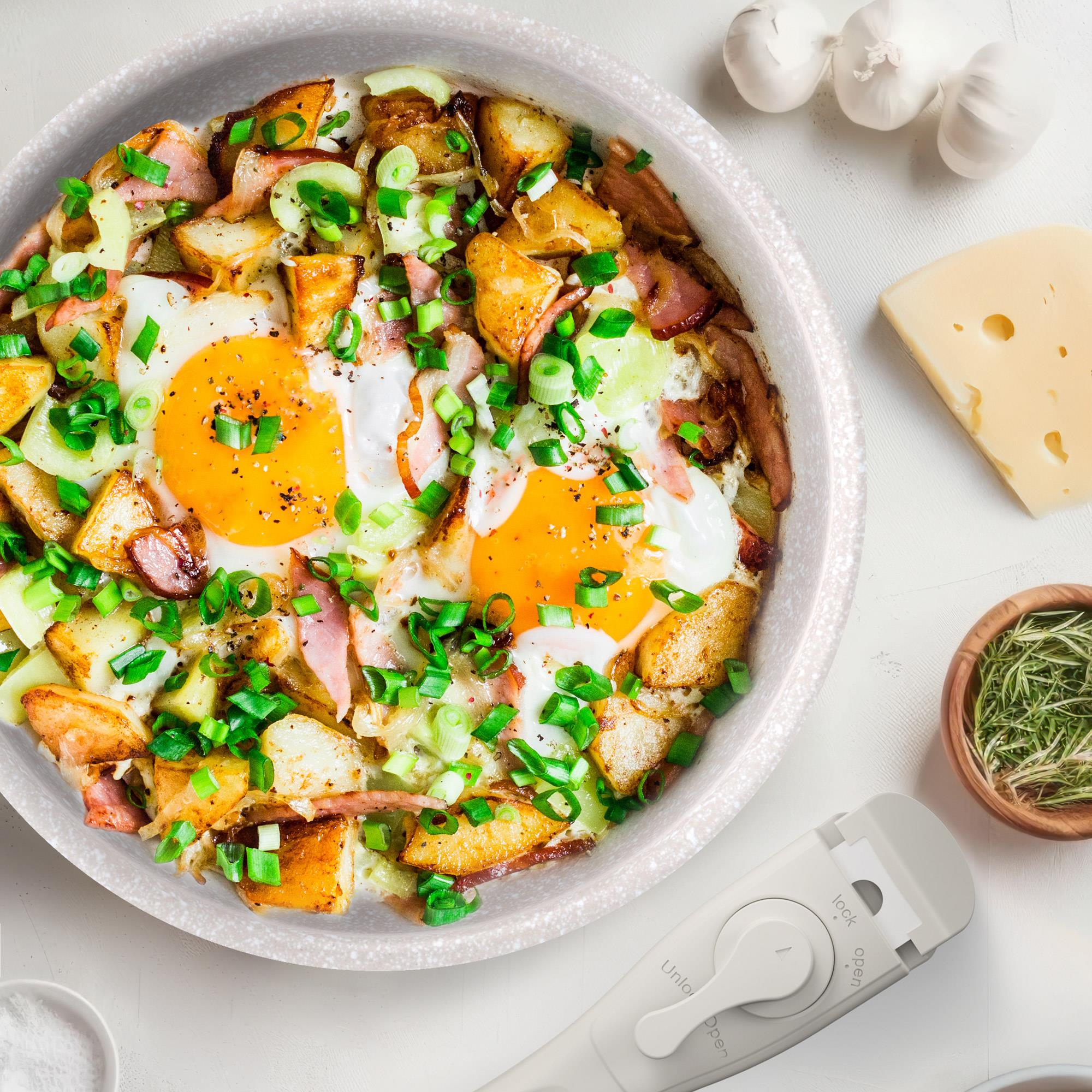 Plato con huevos fritos, patatas, tocino y cebolletas. También hay ajo, queso, hierbas y un abrelatas.
