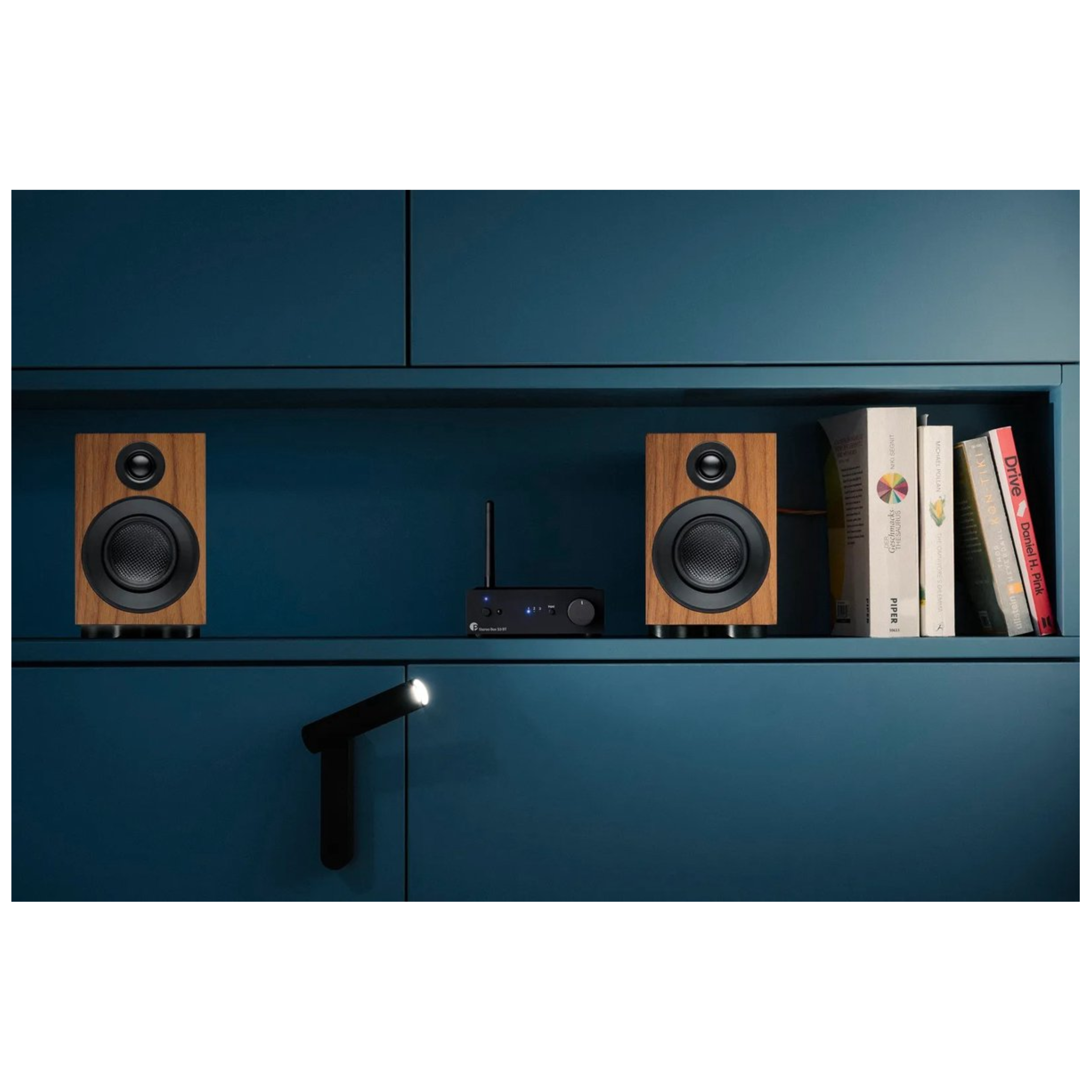 Drewniane głośniki, czarny wzmacniacz, książki i światło na niebieskiej półce.