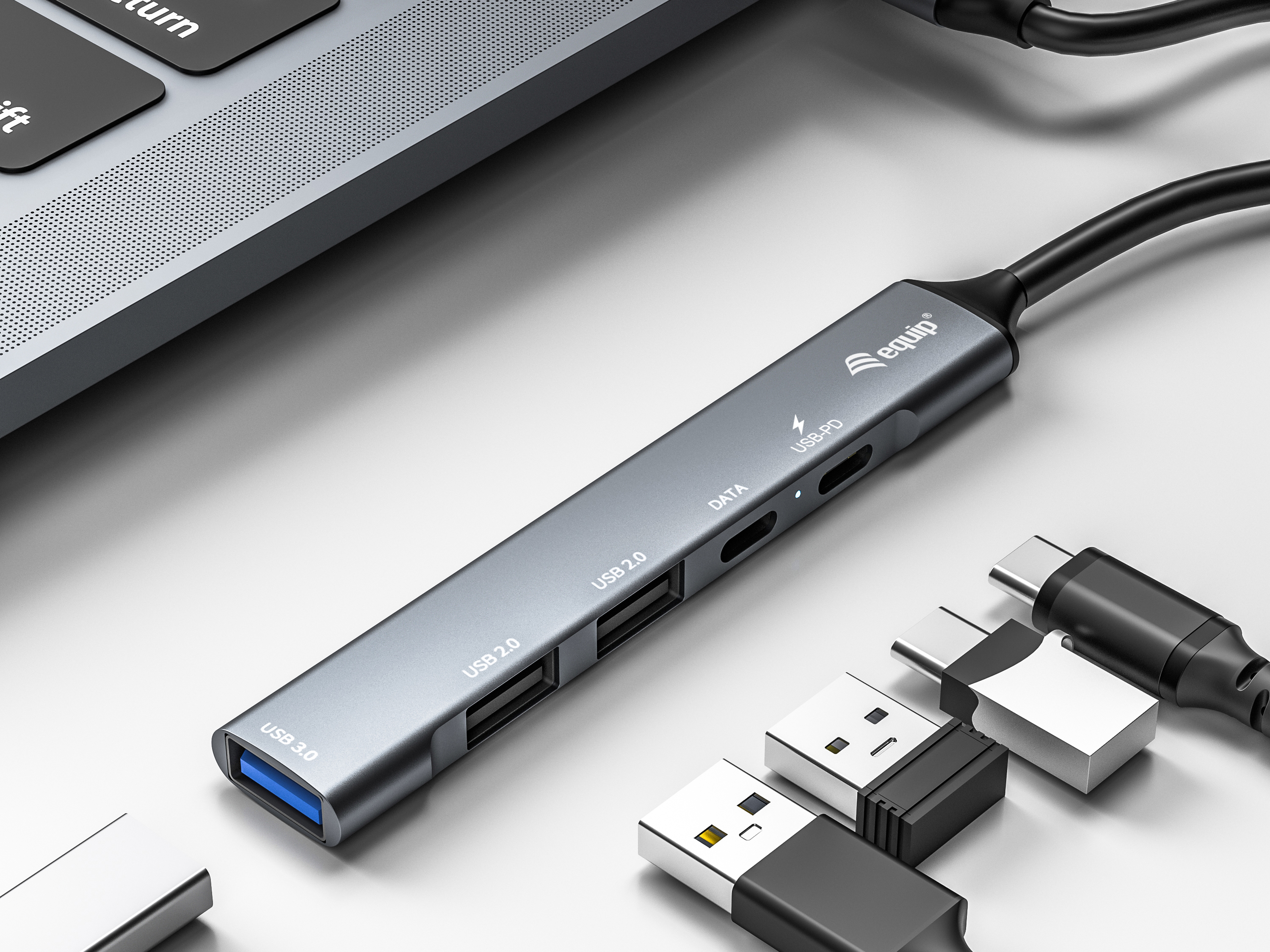 Un concentrador USB gris con varios puertos, cables y conectores sobre una superficie blanca, cerca de un teclado de portátil.