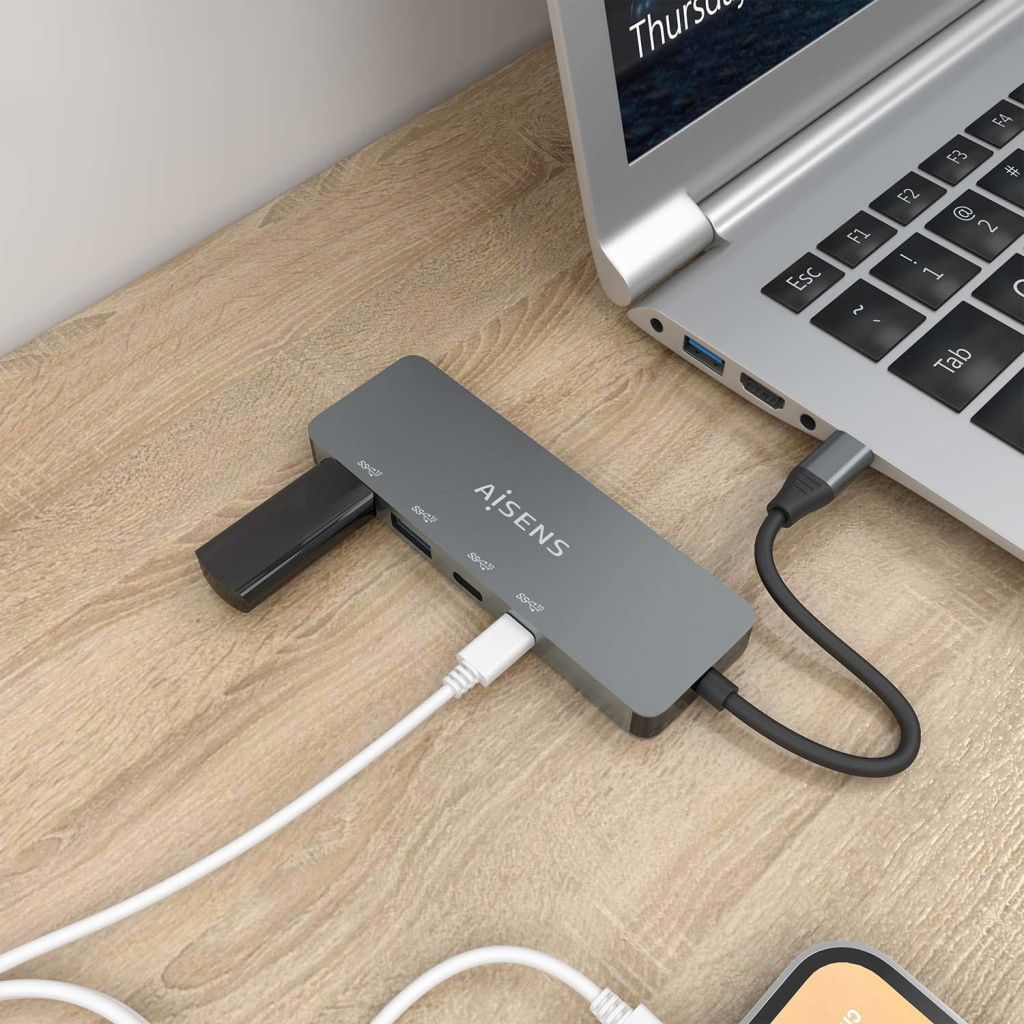 Un hub USB grigio collegato a un laptop. I cavi si collegano all'hub. Un telefono è sul tavolo.