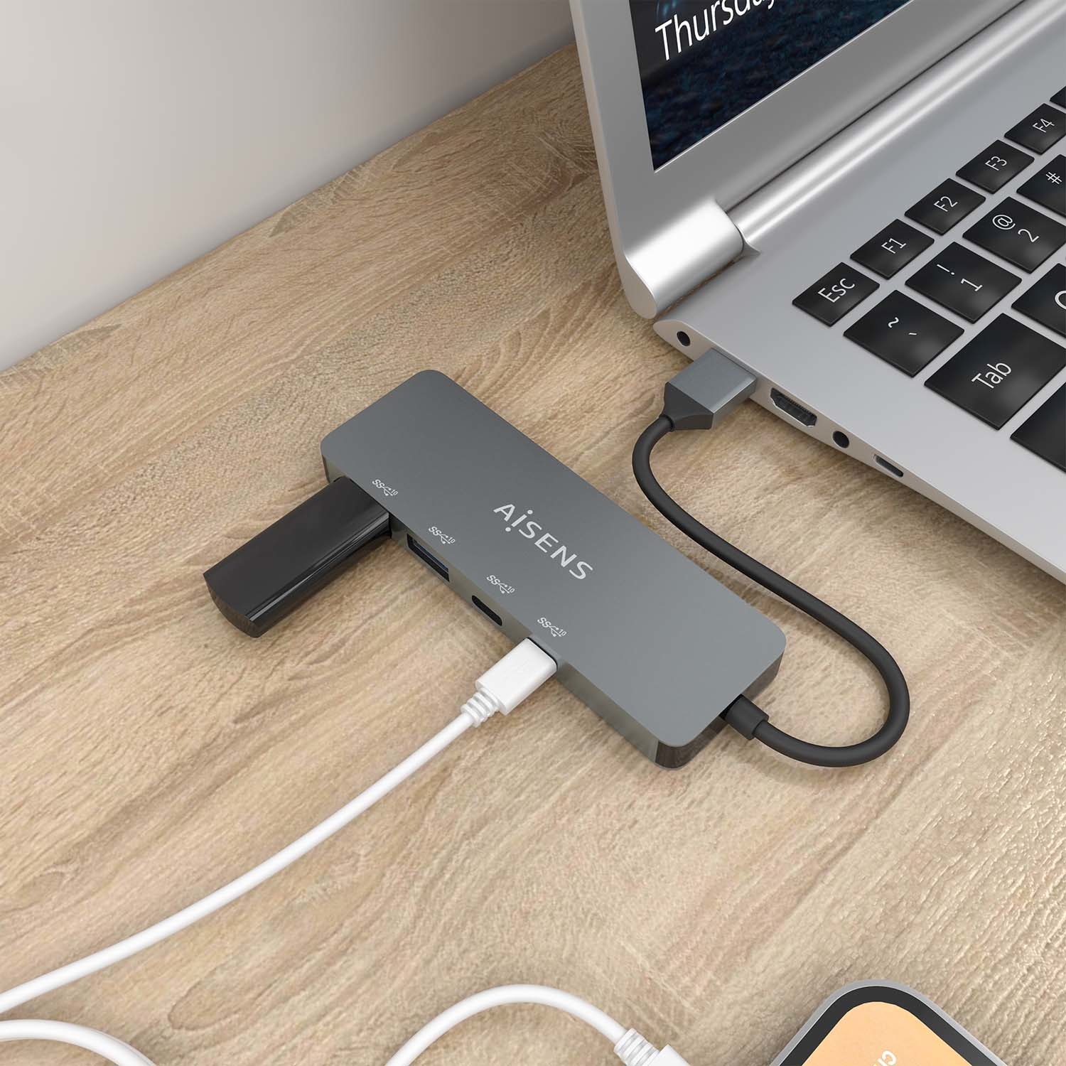 Un concentrador USB gris con cables blancos y negros conectados a una laptop en una superficie de madera.