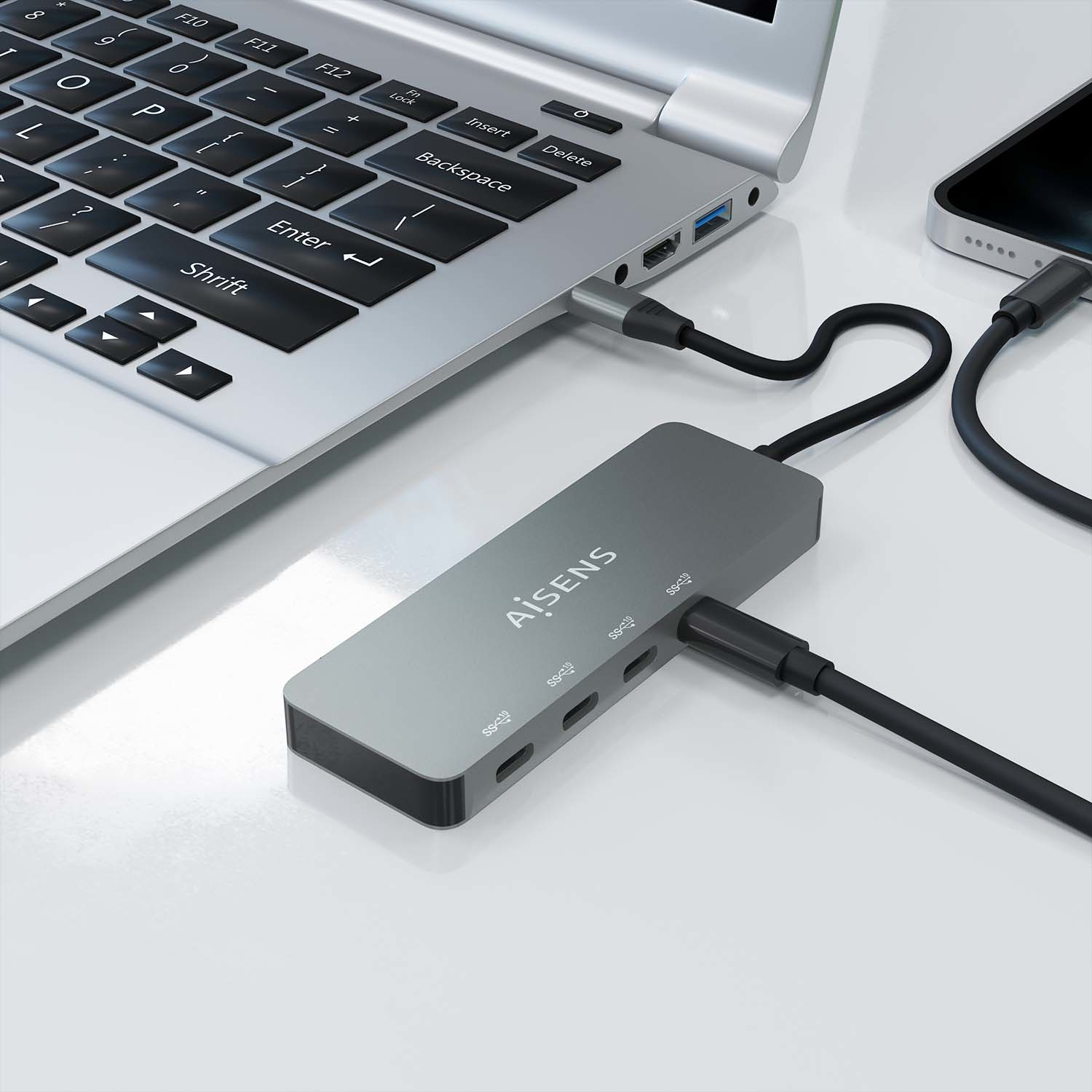 Una computadora portátil está conectada a un concentrador USB gris, que también está conectado a un teléfono. Los cables conectan los tres dispositivos.