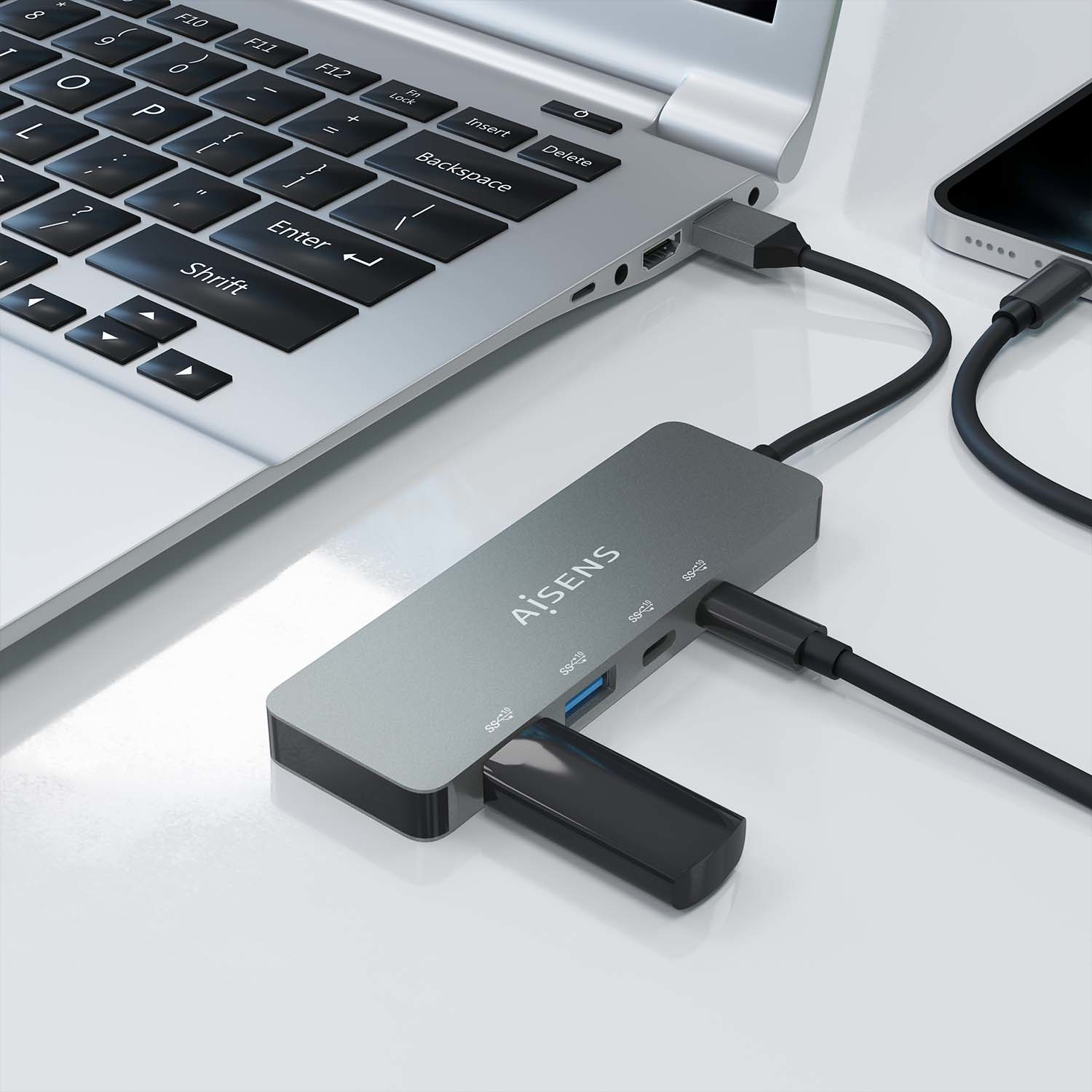 Una laptop conectada a un concentrador y un teléfono. El concentrador está conectado a través de USB-C. Cables y dispositivos sobre superficie blanca.