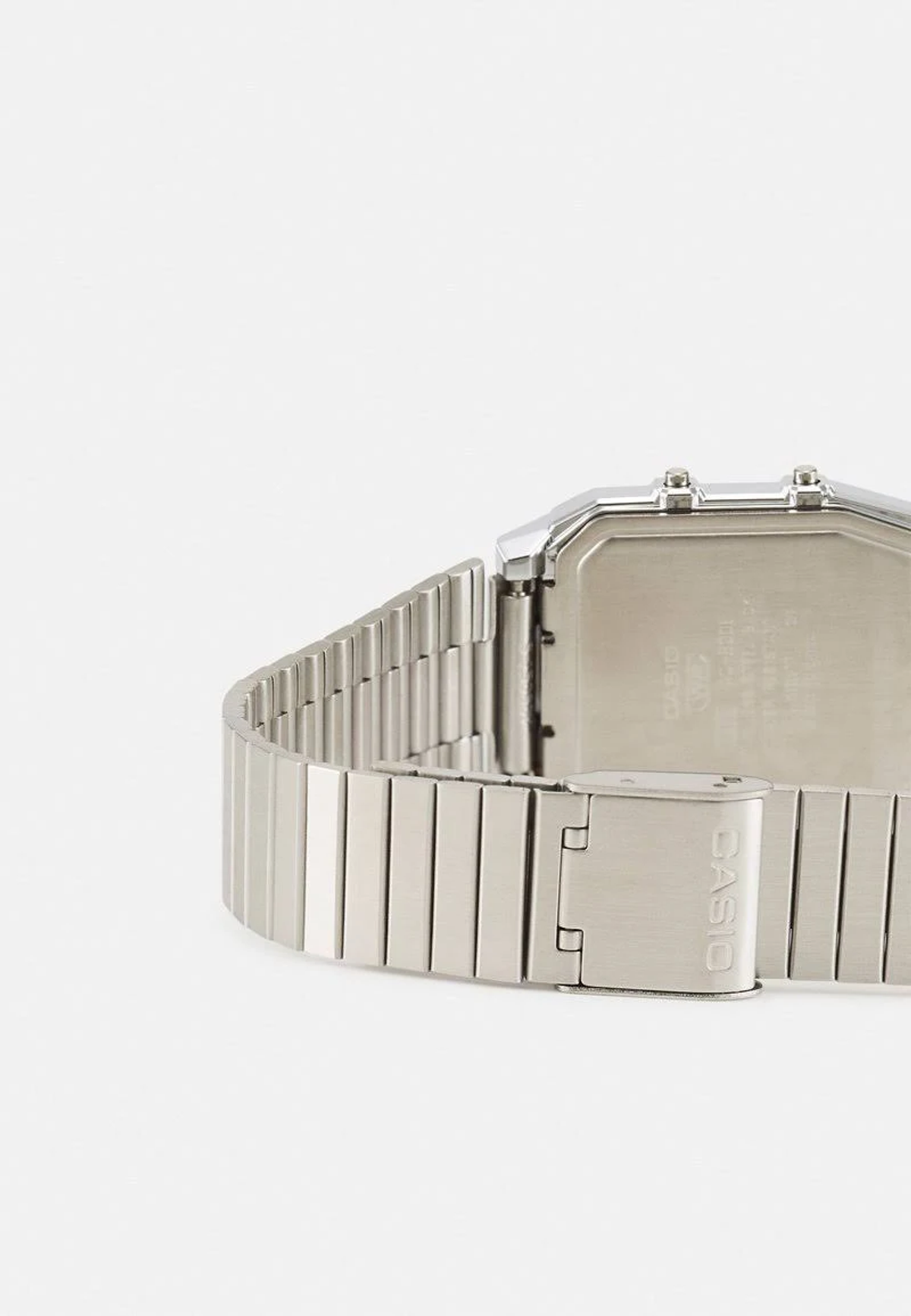 Primer plano de un reloj Casio plateado. La correa del reloj es de metal. La esfera del reloj es rectangular. El fondo es blanco.