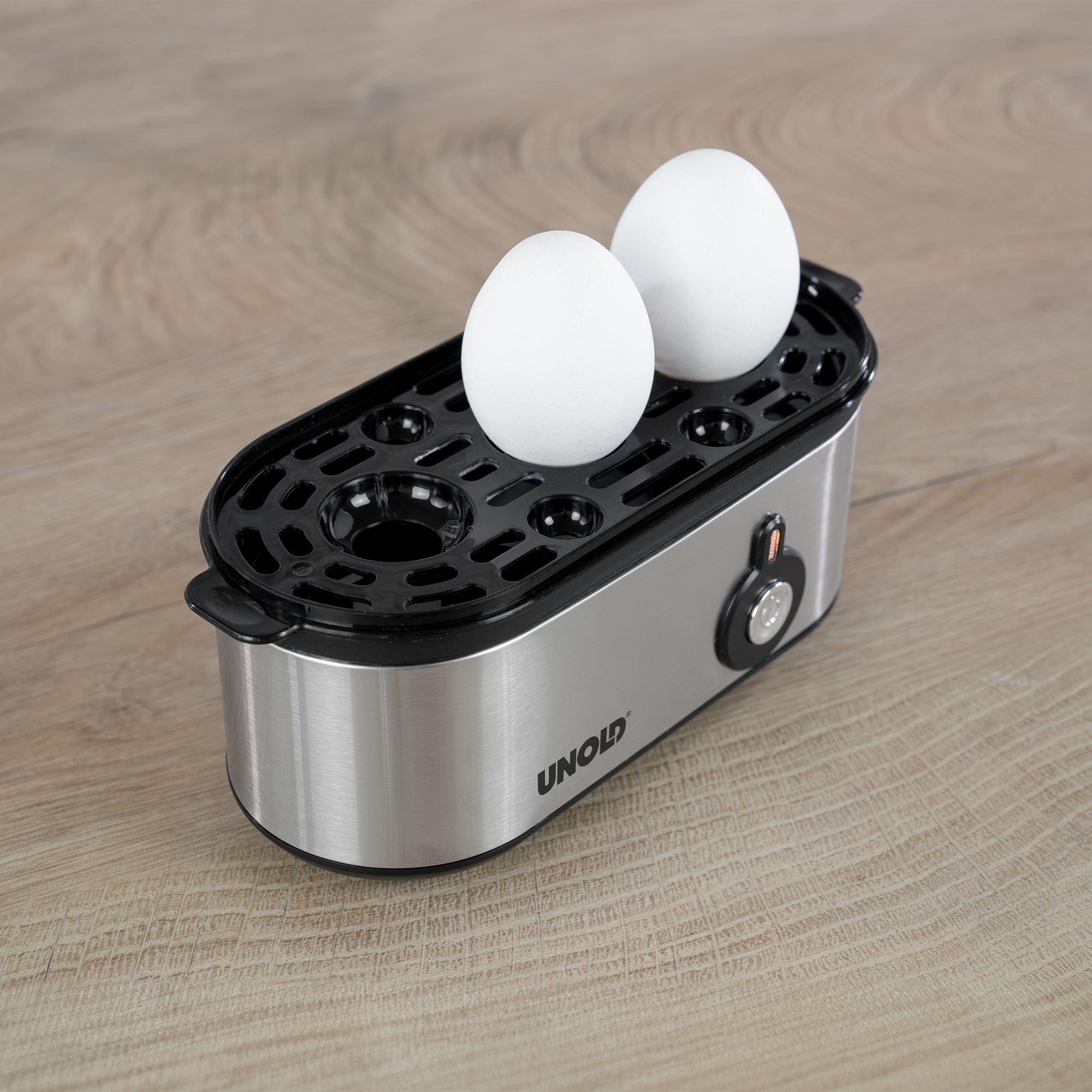 Urządzenie do gotowania jajek z dwoma białymi jajkami na górze. Stoi na drewnianej powierzchni.