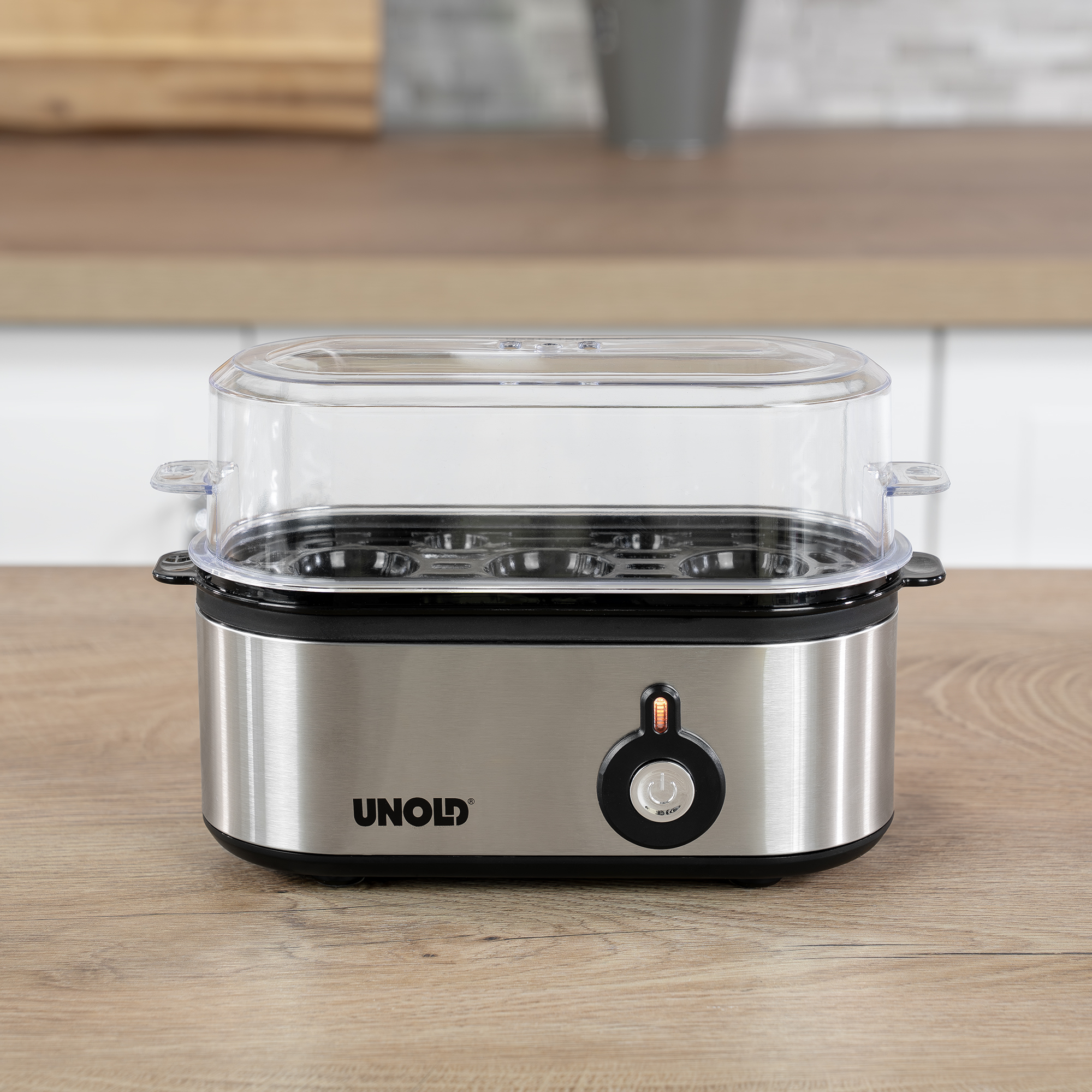 Gotowacz do jajek ze srebra i czerni, z przezroczystą pokrywą. Stoi na drewnianej powierzchni.