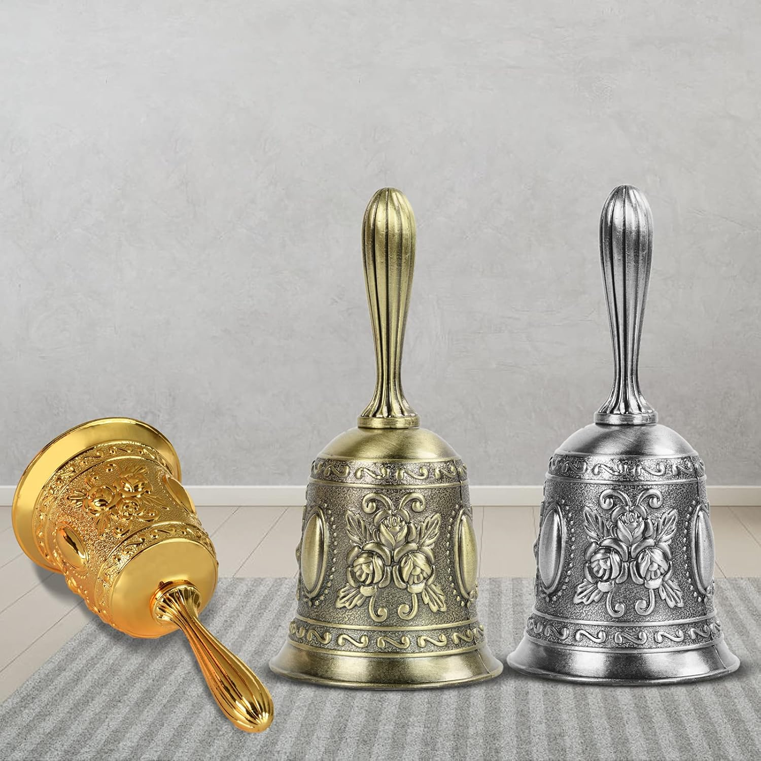 Drei dekorative Glocken. Eine goldene Glocke liegt auf der Seite. Die anderen stehen aufrecht, eine goldene und eine silberne, alle mit Blumendesigns.