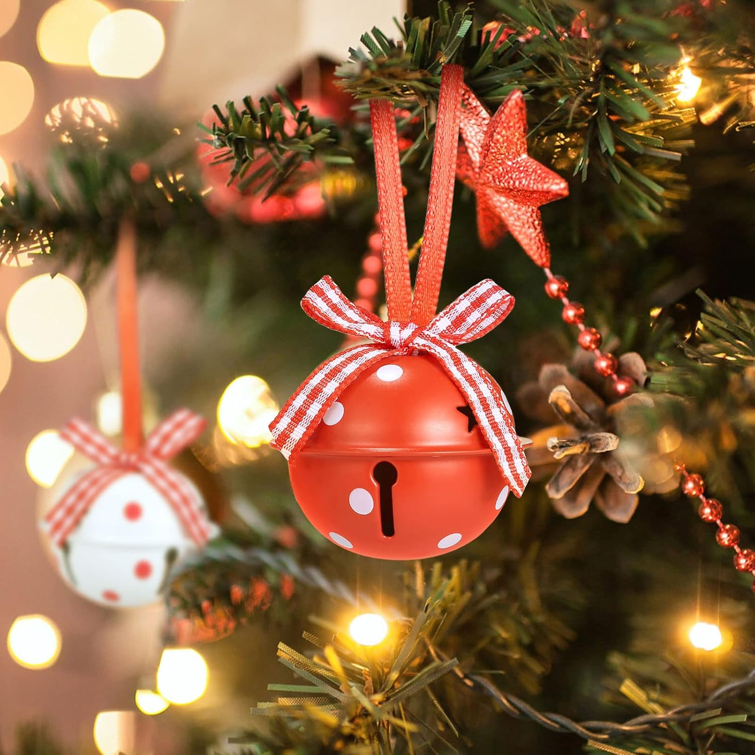 Nahaufnahme eines Weihnachtsbaums mit roten Glockenornamenten, einem Stern und Lichtern. Eine Glocke hat weiße Punkte und eine rot-weiße Schleife.