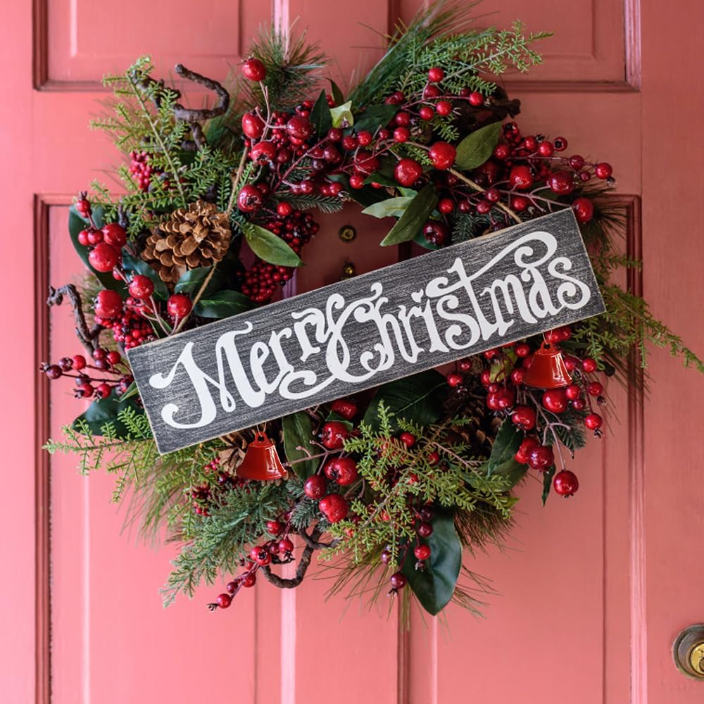 Ein Weihnachtskranz an einer rosa Tür. Er hat rote Beeren, grüne Blätter und ein Schild mit der Aufschrift 'Merry Christmas'.