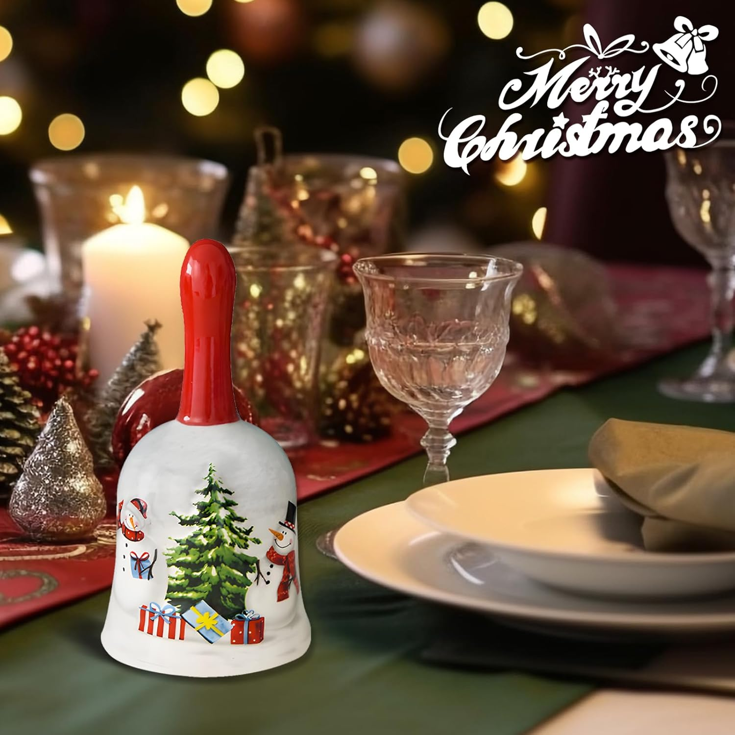 Eine Weihnachtsglocke mit rotem Griff steht auf einem für das Abendessen gedeckten Tisch. Auf der Glocke sind Schneemänner und ein Weihnachtsbaum abgebildet.
