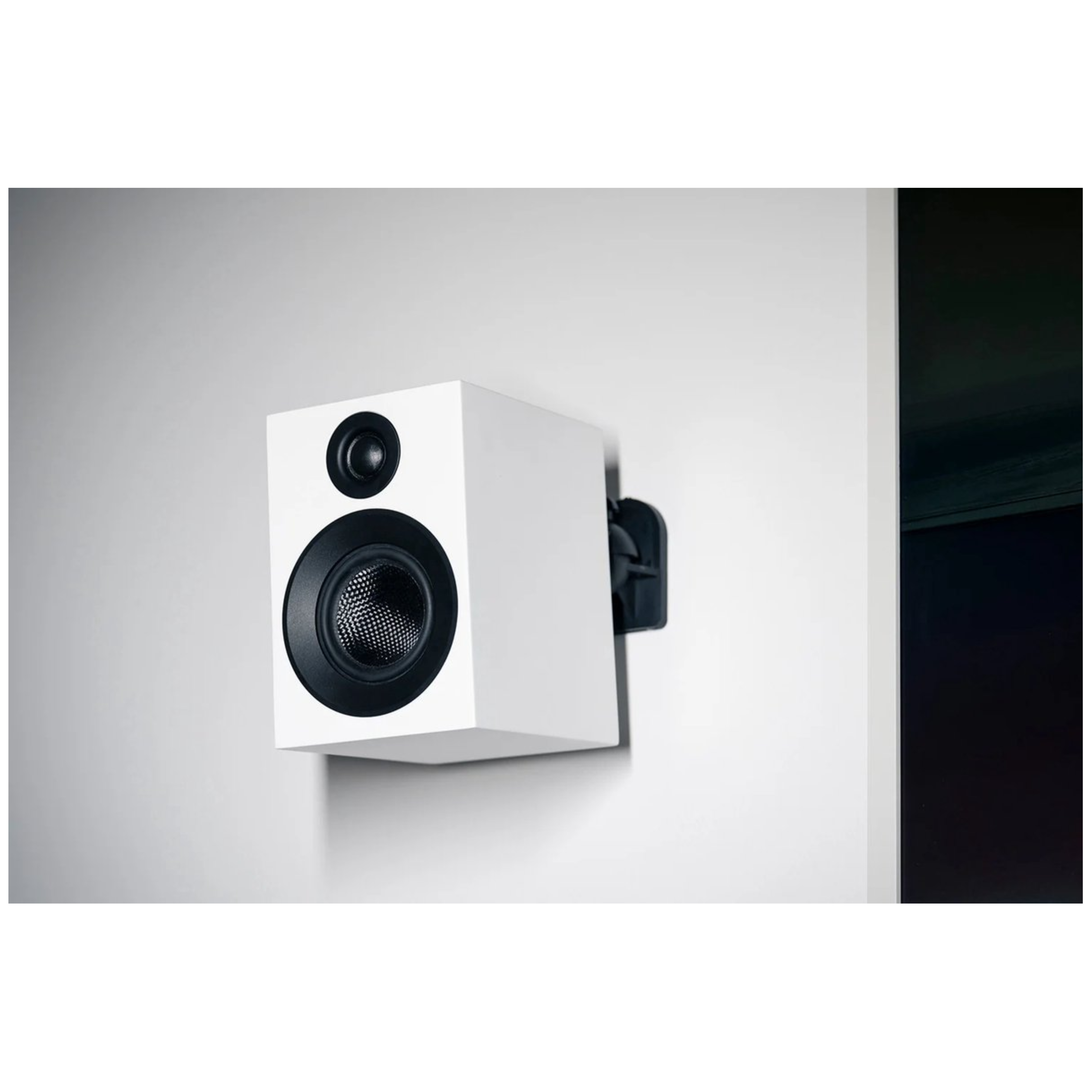 Biały głośnik z czarnymi elementami zamontowany na białej ścianie. Czarna ściana po prawej.