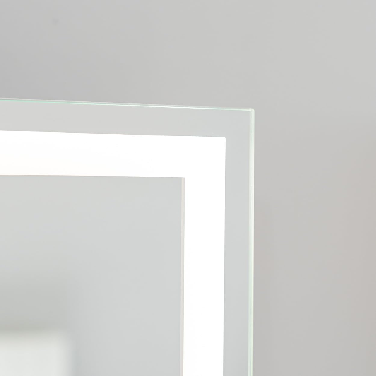 Primer plano de un marco rectangular blanco e iluminado. El marco está contra una pared gris claro. Se ve la esquina.
