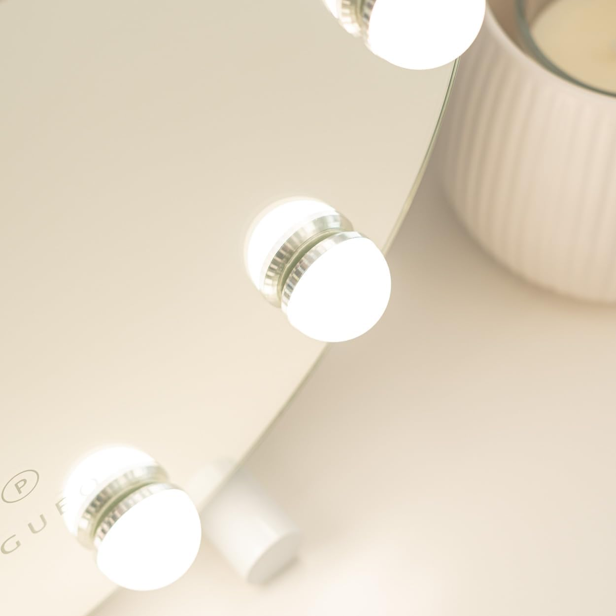 Espejo de maquillaje con luces brillantes. Un portavelas blanco a la derecha. Espejo en ángulo. Iluminación suave y cálida.