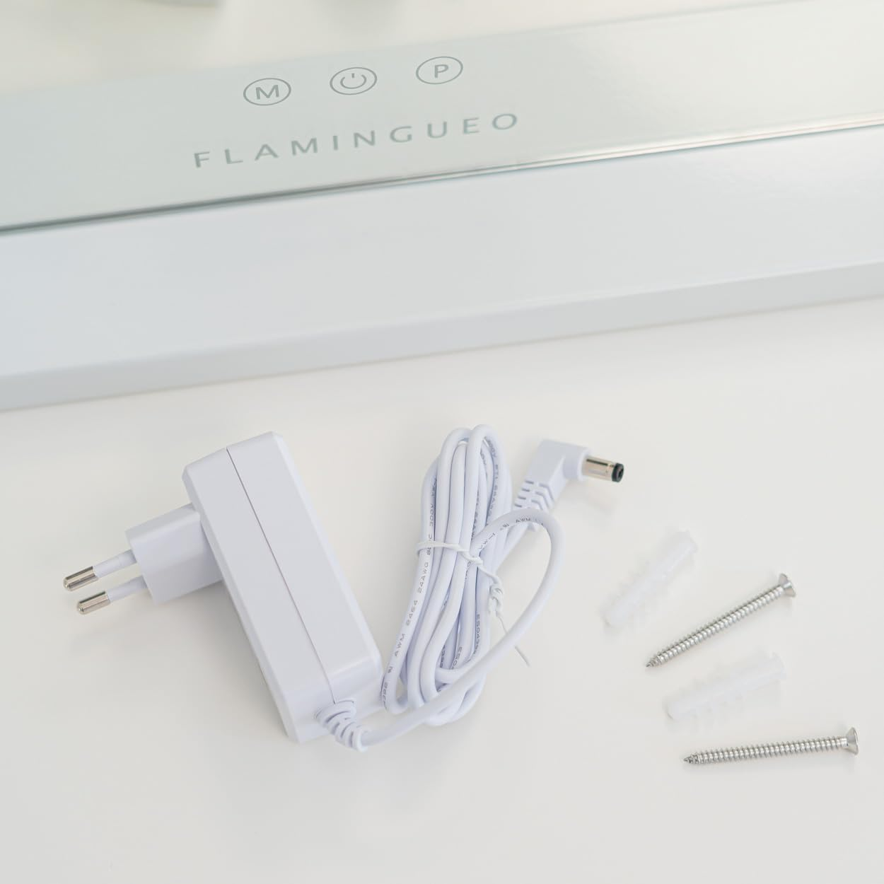 Adaptador de corriente blanco, cable, tornillos y una lámpara con la marca FLAMINGUEO. Todos los objetos están sobre una superficie blanca.