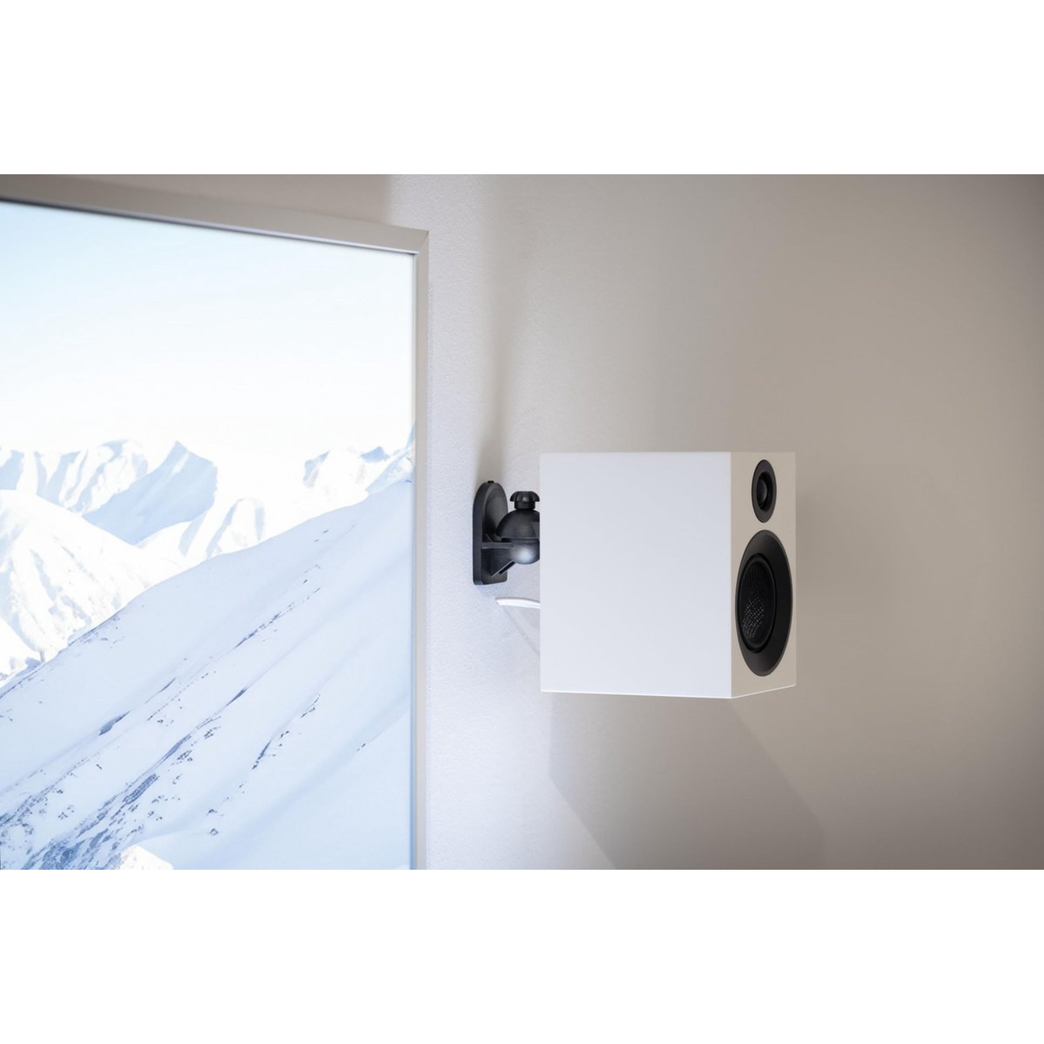 Biały głośnik zamontowany na ścianie. Okno z widokiem na ośnieżone góry.