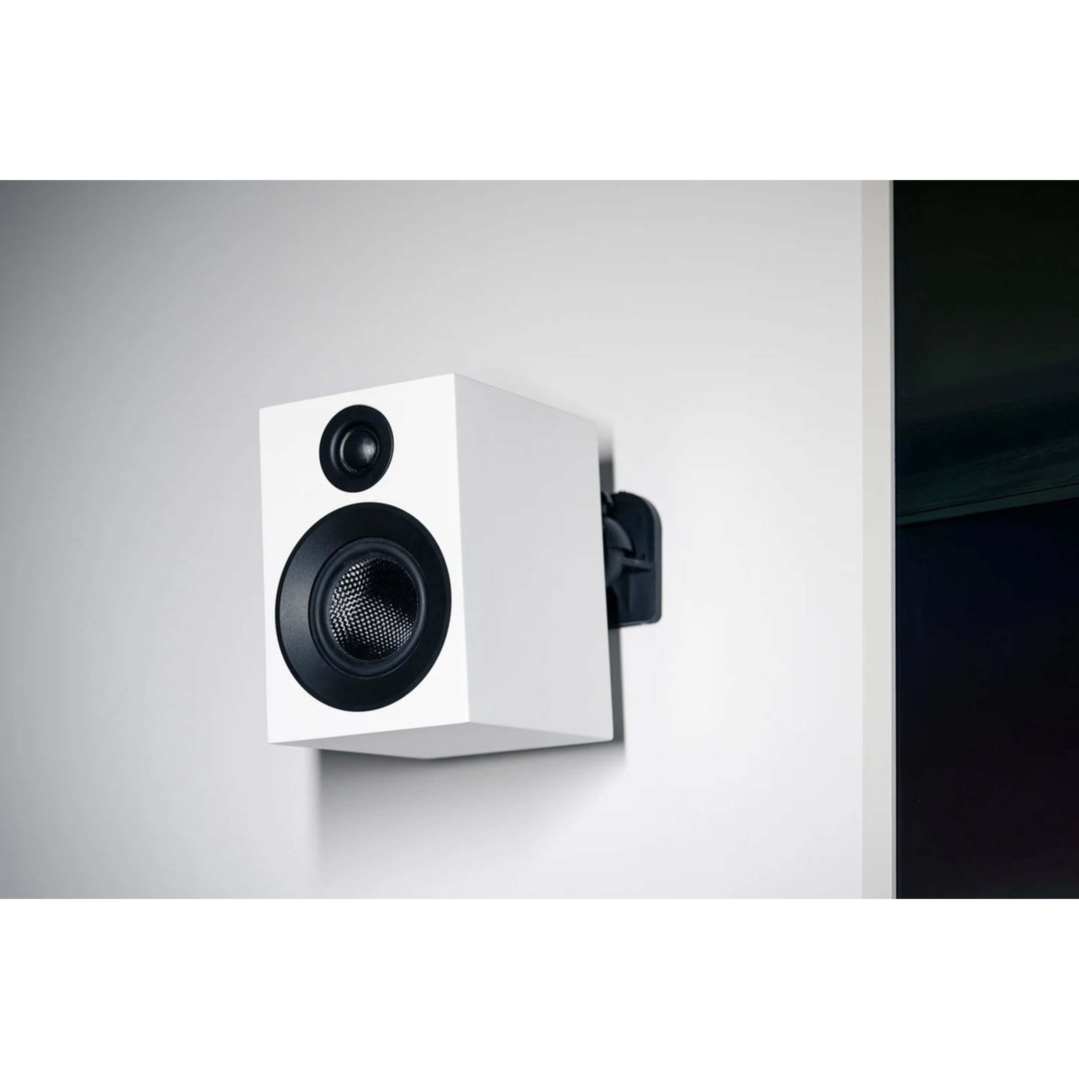 Biały głośnik z czarnymi elementami zamontowany na białej ścianie. Tło to biała ściana.